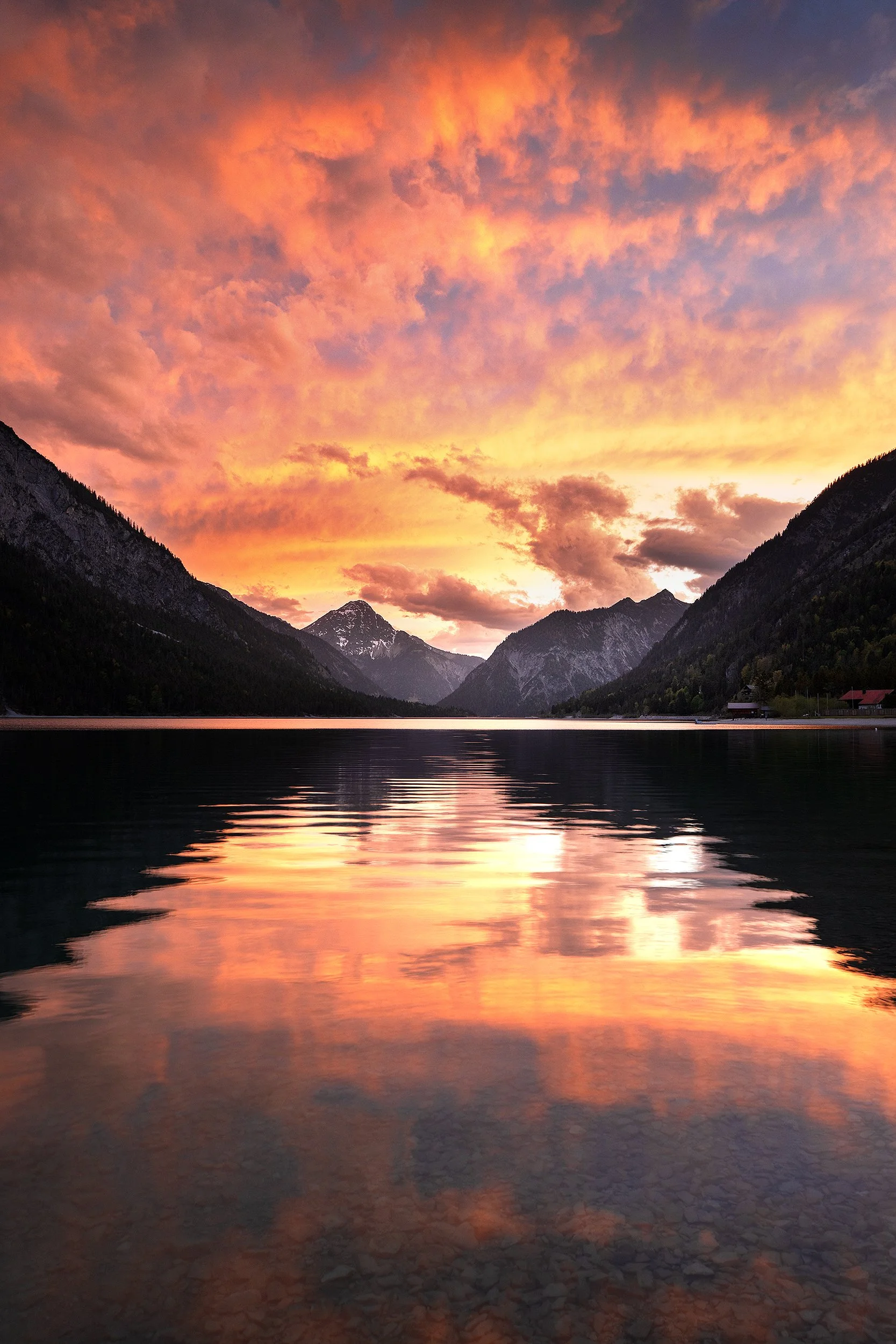 A mountain lake during sunset with a vibrant orange and pink sky, reflecting on the water.