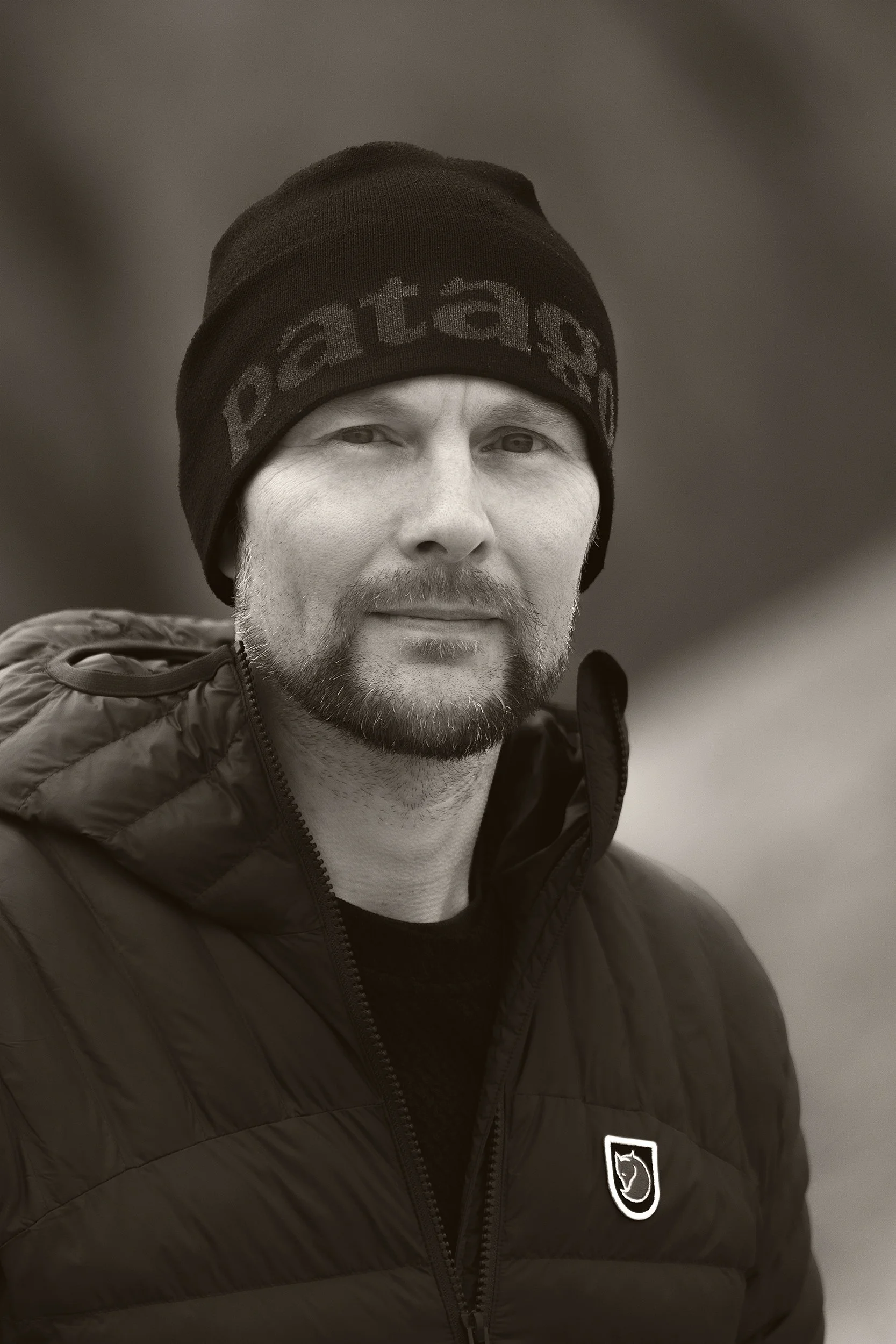 A man wearing a beanie hat and a black puffy jacket, looking at the camera with a slight smile.