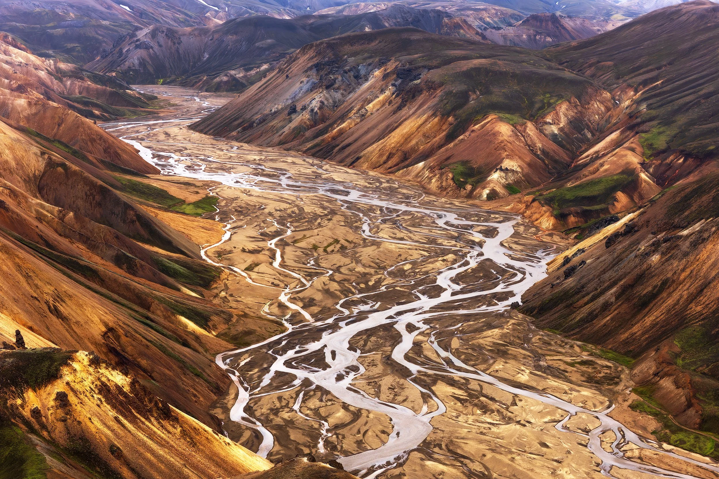 Aerial view of a mountainous valley with multicolored, rugged hills and multiple winding rivers running through the dried lakebed.