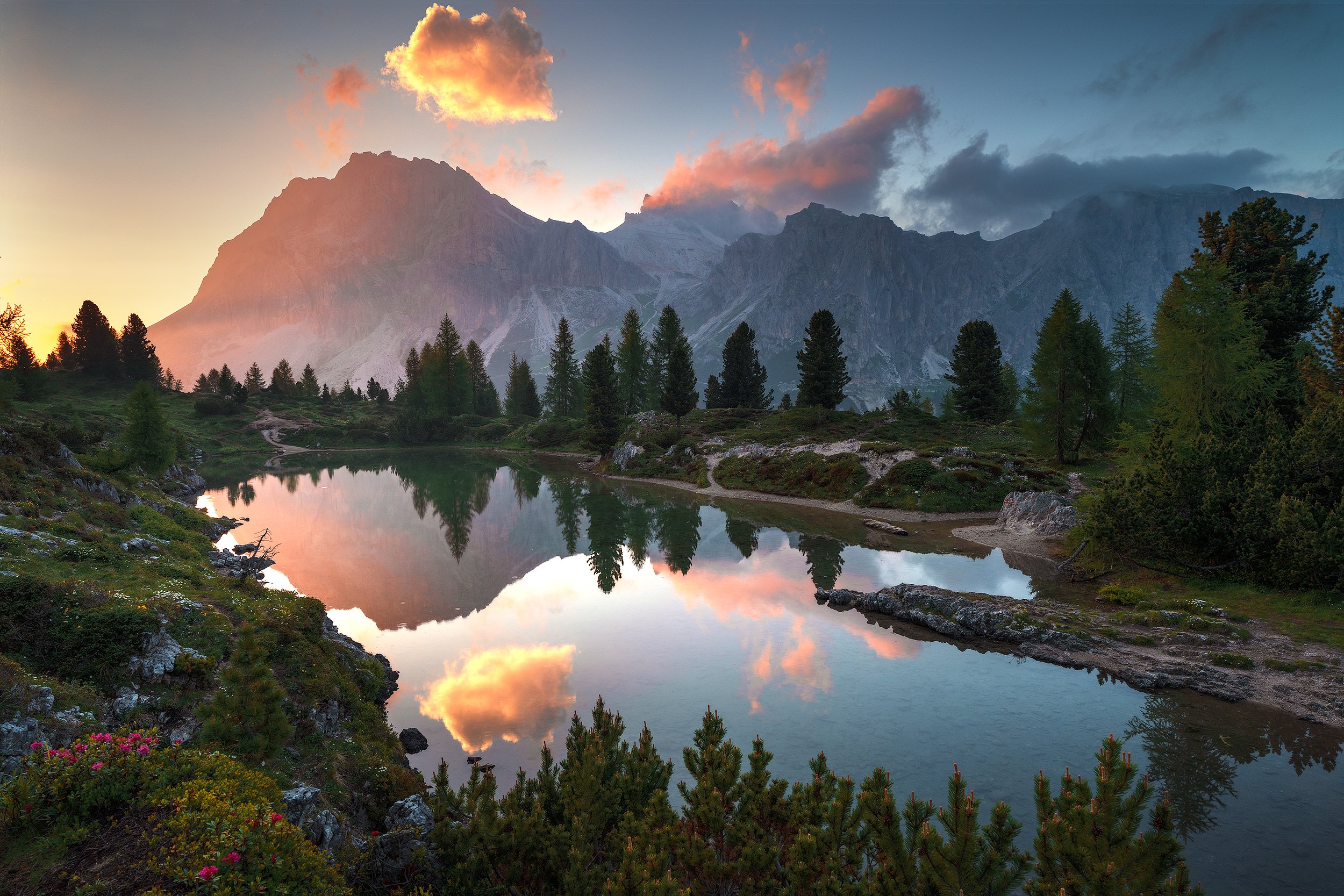 ID-201-IT 

Scenic mountain landscape at sunset, with a peaceful lake reflecting the colorful sky, tall pine trees, and rugged mountains in the background.