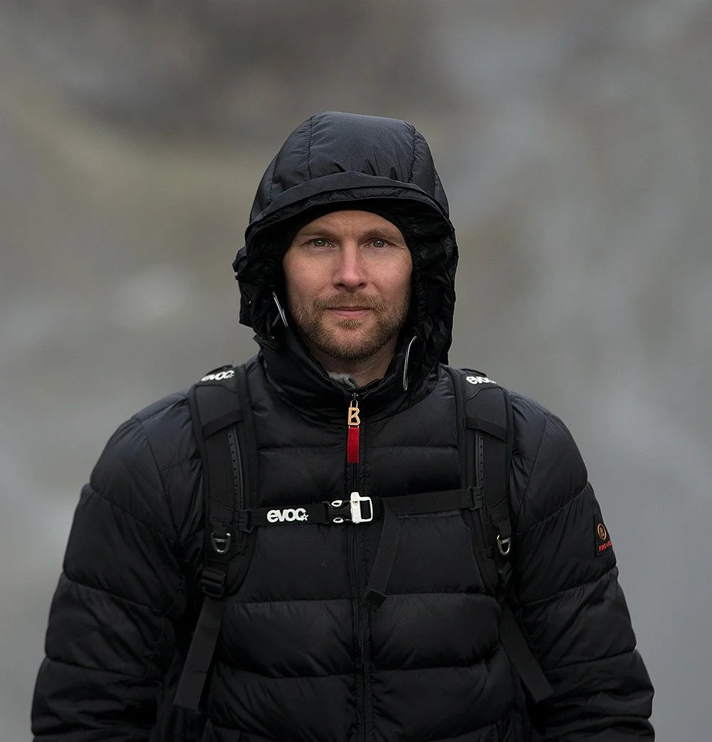 Man dressed in black outdoor gear standing in a misty mountain landscape.