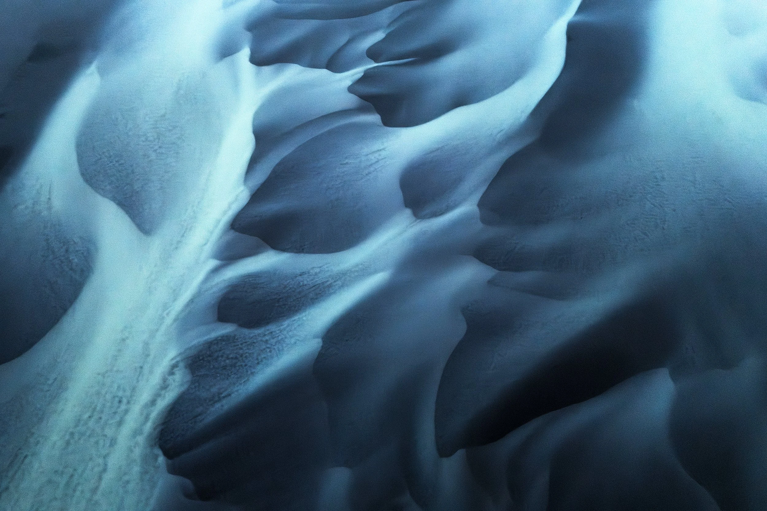 Close-up of snow and ice formations with smooth, curved surfaces and textured details in shades of blue and white.