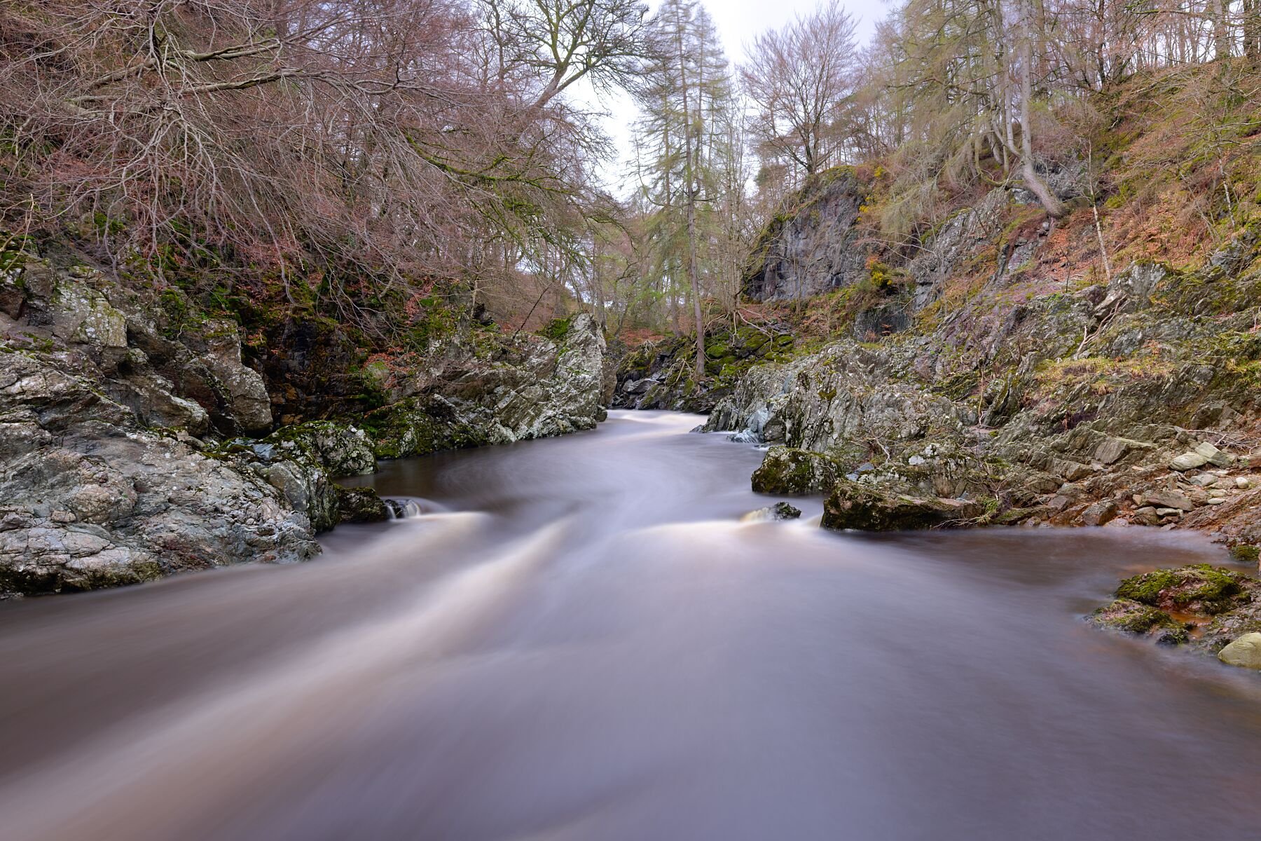 A quiet stretch of the River North Esk becomes a place of stillness and movement all at once. The long‑exposure flow softens into a silken ribbon, winding its way through rugged rocks and bare trees. Moss clings to the stone like a memory of warmer s