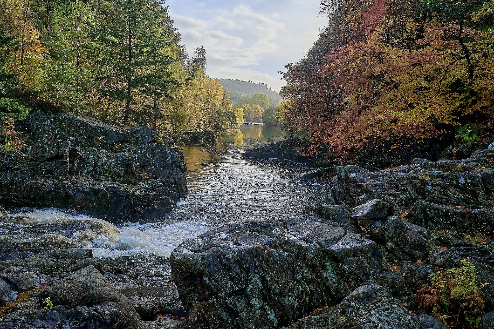 Along the River Garry at Killiecrankie, the landscape shifts from deep evergreen shade to the firelit glow of autumn. Water gathers speed over ancient rocks, catching the season’s colours as it moves. This photograph holds the quiet power of the High