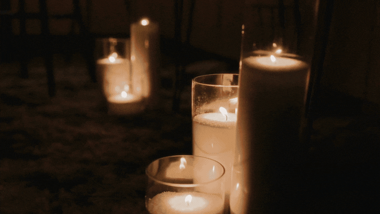 Five lit candles of varying heights on a dark surface, creating a warm glow.