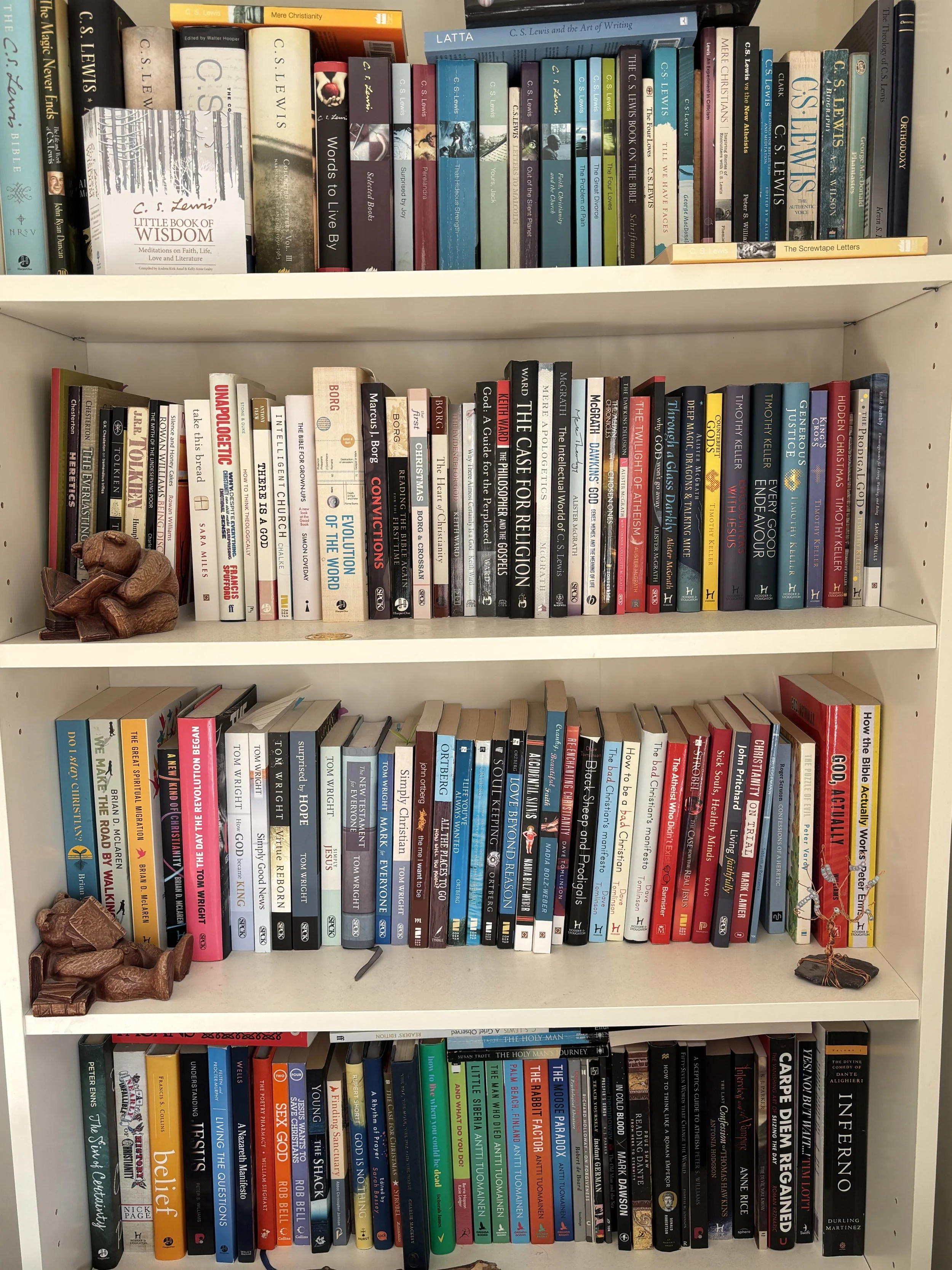 Bookshelves filled with various books, including titles on religion, philosophy, and literature, along with decorative items like a small sculpture of a reclining figure on the left side.
