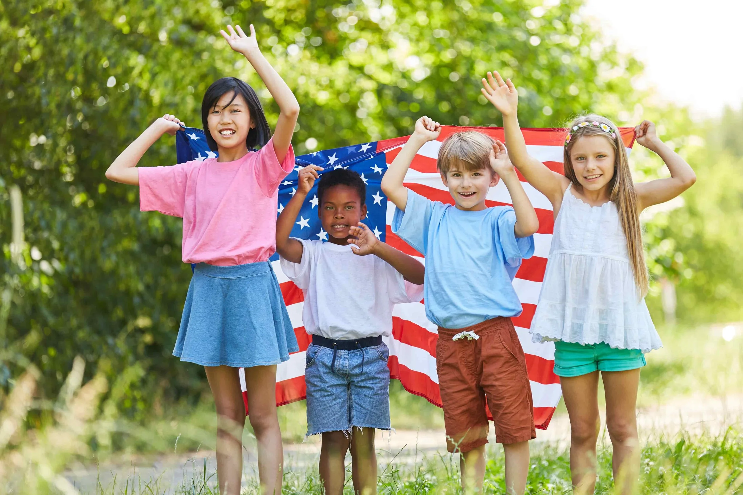 Group of children smiling and holding an American flag outdoors