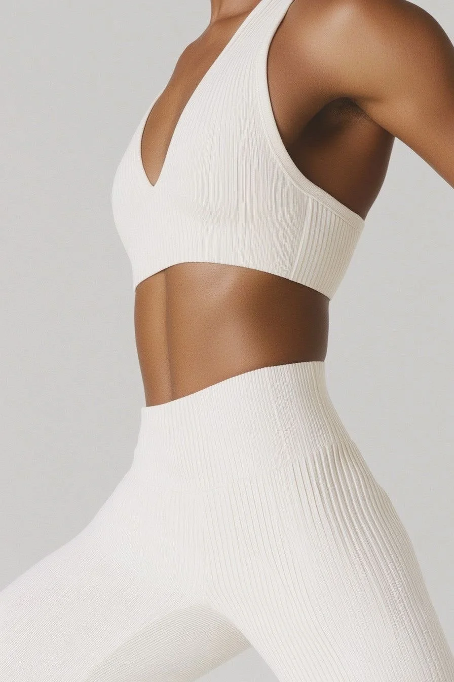 Close-up of a woman's torso in a white athletic top and high-waisted leggings with a ribbed texture.