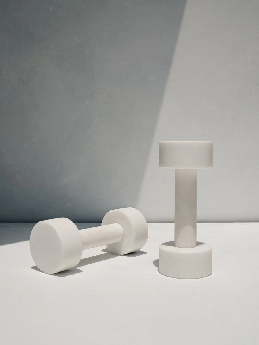 Two white cylindrical dumbbells on a white surface, with one standing upright and the other lying down, casting soft shadows.