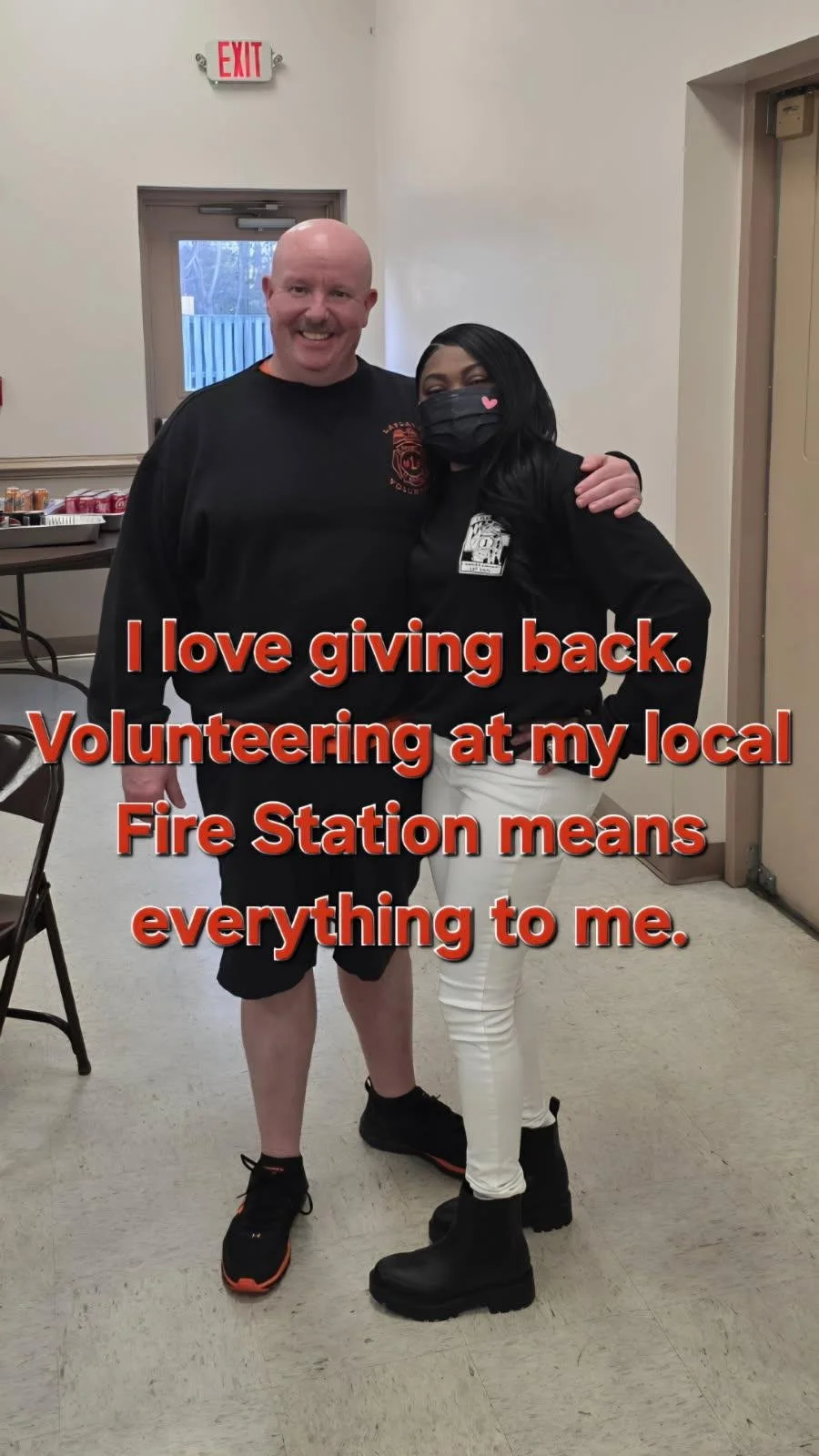 A man and woman standing together indoors, smiling. The woman is wearing a face mask with a pink heart, and the man has a bald head and a mustache. There is a table with cans in the background. Overlaid text says, 'I love giving back. Volunteering at