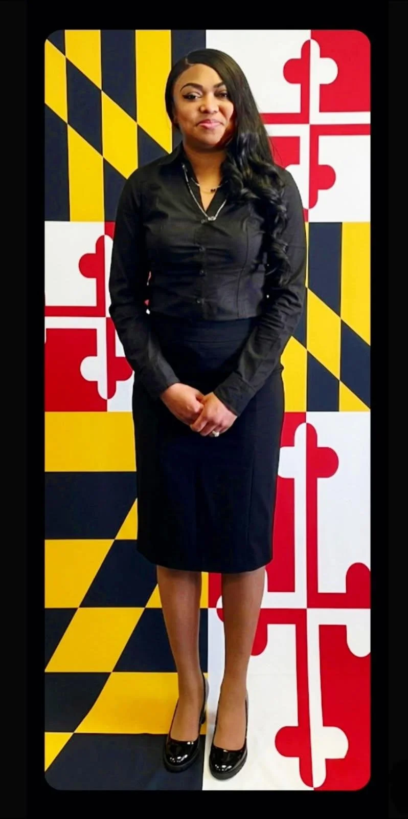 A woman in black professional attire standing in front of a background featuring the Maryland state flag.
