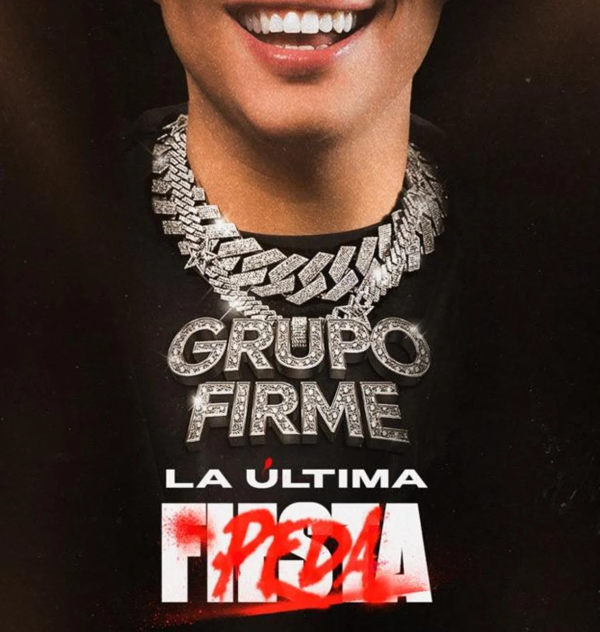 Close-up of a person smiling wearing a large diamond-encrusted necklace with the words "GRUPO FIRME" and a black shirt with Spanish text in red and white.