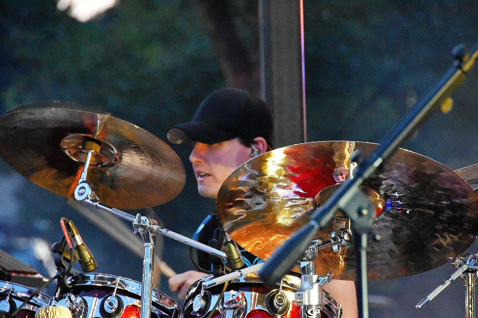 A man wearing a black cap and headphones playing a drum set with cymbals.