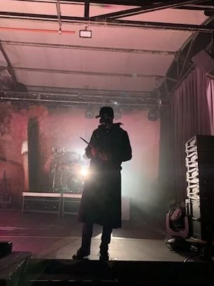 A silhouette of a drummer on a stage with stage lights, and a backdrop with curtains.