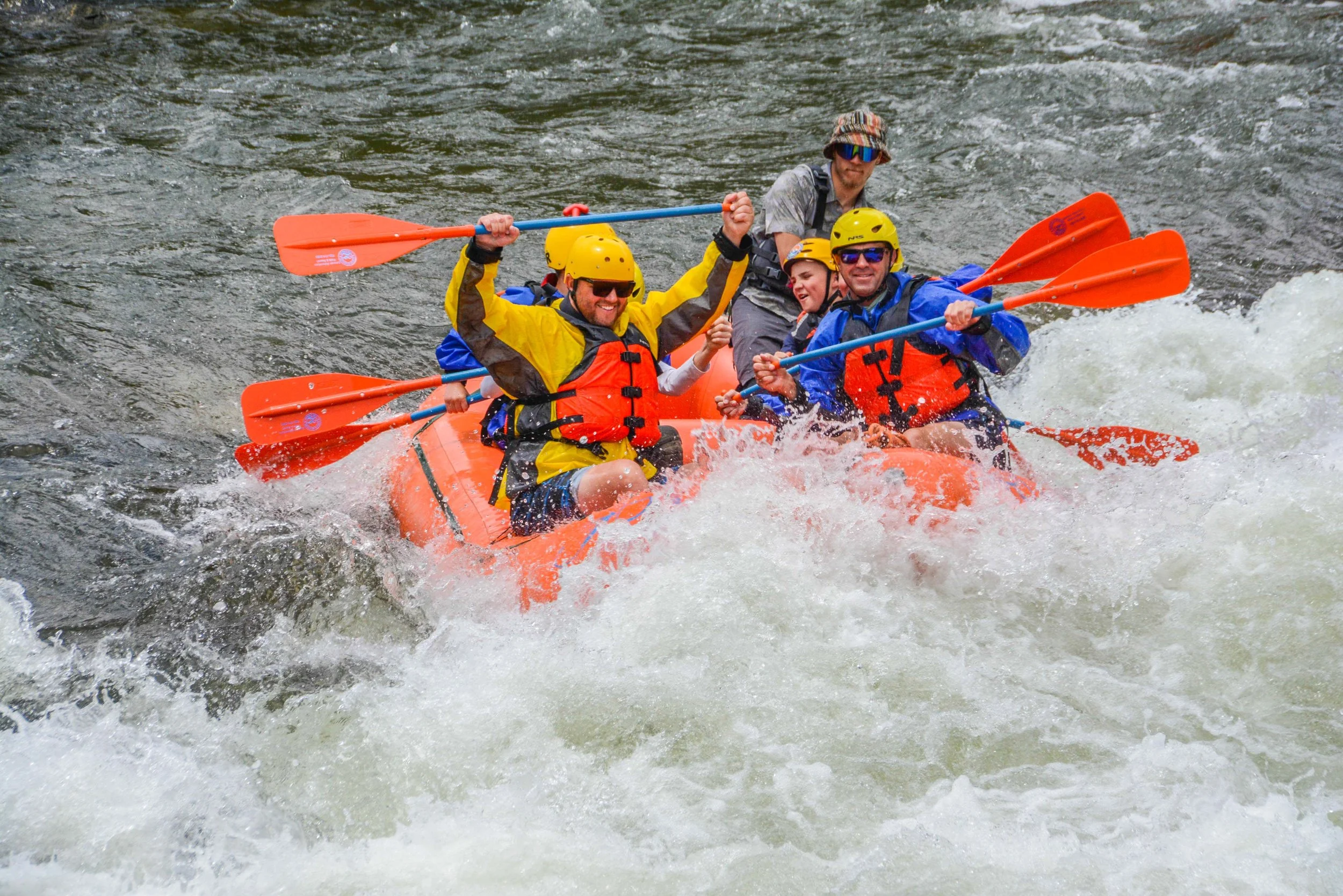 A group of five people wearing helmets and life jackets white water rafting on a river.