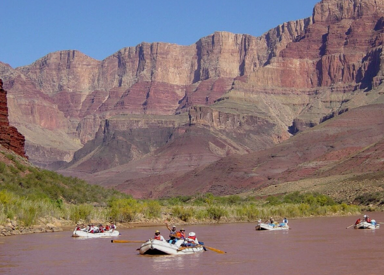 Tourists in boats floating on the Colorado River with the Grand Canyon in the background.