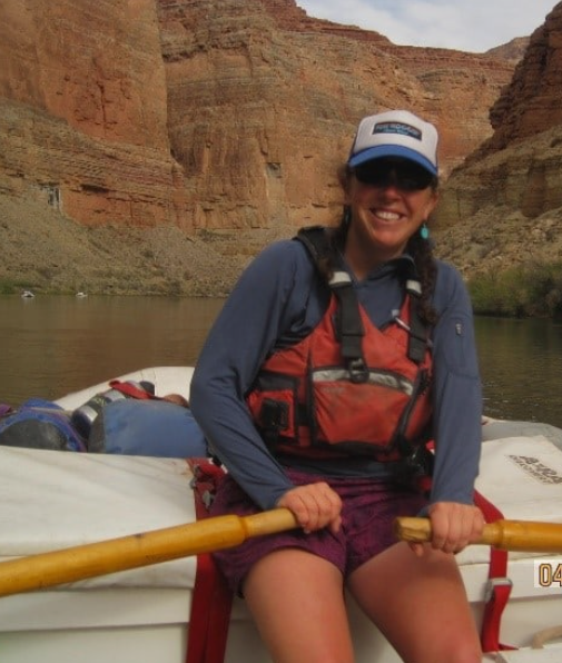 Woman smiling on a boat in a canyon with water, red rock cliffs, and a cloudy sky, Professional guided rapid rafting tours at Idaho Springs Rafting Company, Colorado