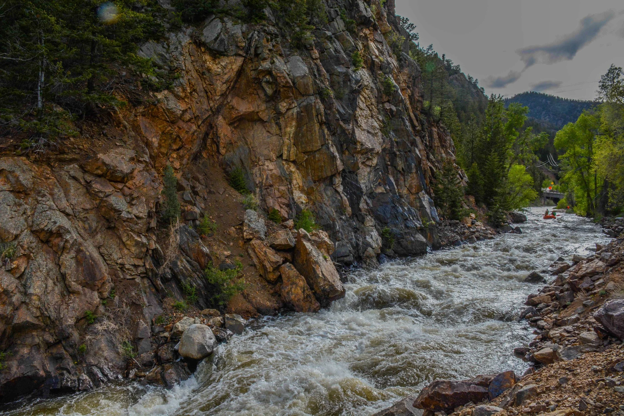 A rushing mountain river flowing through a rocky canyon surrounded by green trees and hills.
