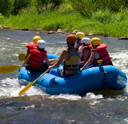 Group of six people, including children and an adult, rafting on a river with greenery in the background.