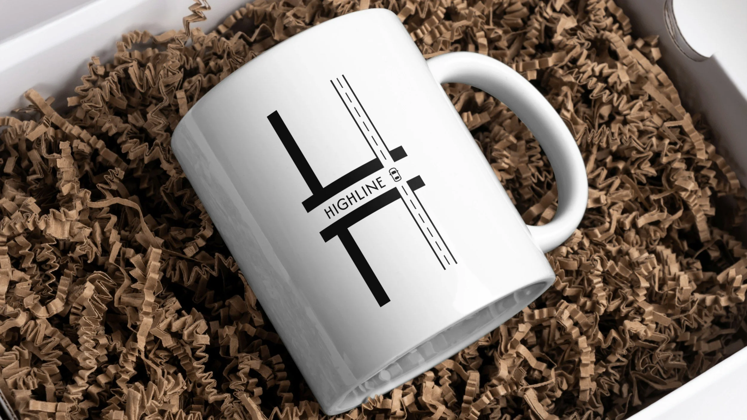 A white coffee mug with black text and graphics resting on crinkled brown paper packaging material.