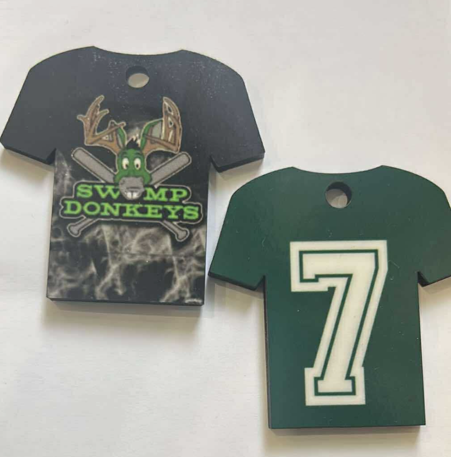 Two foam cutouts of sports jerseys, one black with a shamrock and crossed baseball bats and the words 'Swamp Donkeys,' and the other green with a large white number 7.