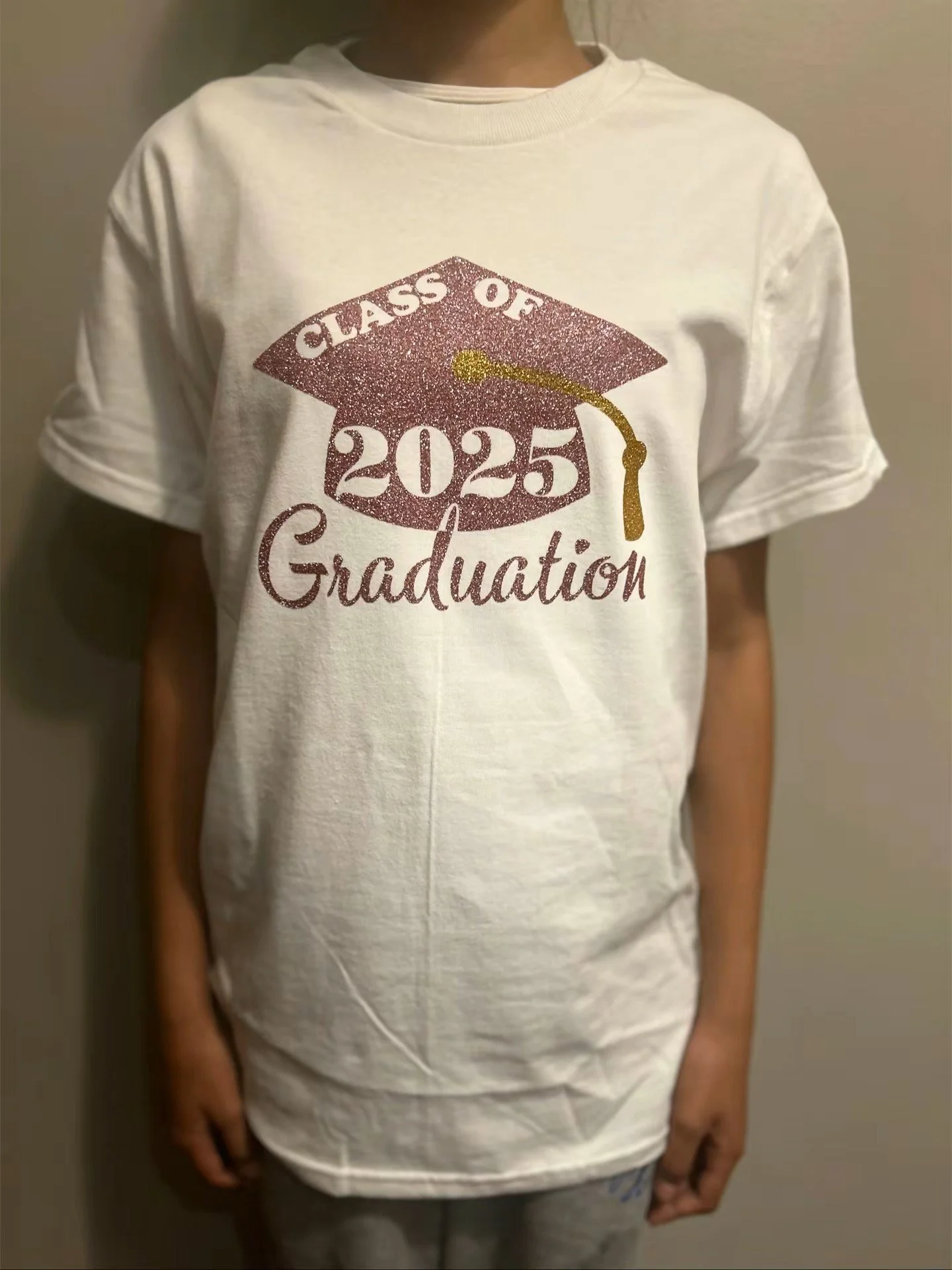 Children's white T-shirt with a glittery maroon graduation cap design that reads "Class of 2025" and a gold tassel, with the word "Graduation" written below.