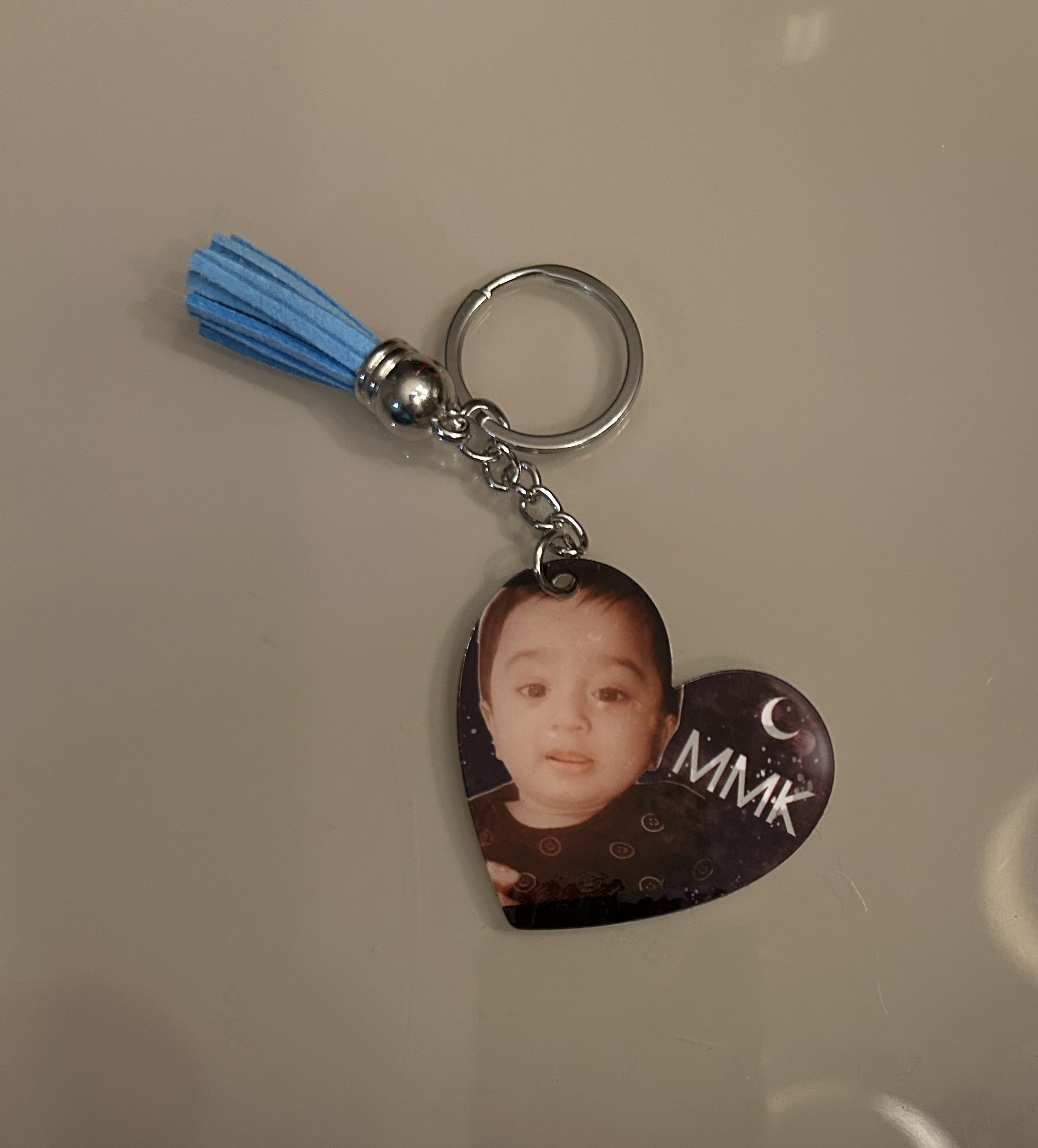 A keychain with a blue tassel and a round black photo holder featuring a young boy's face, attached to a chain.