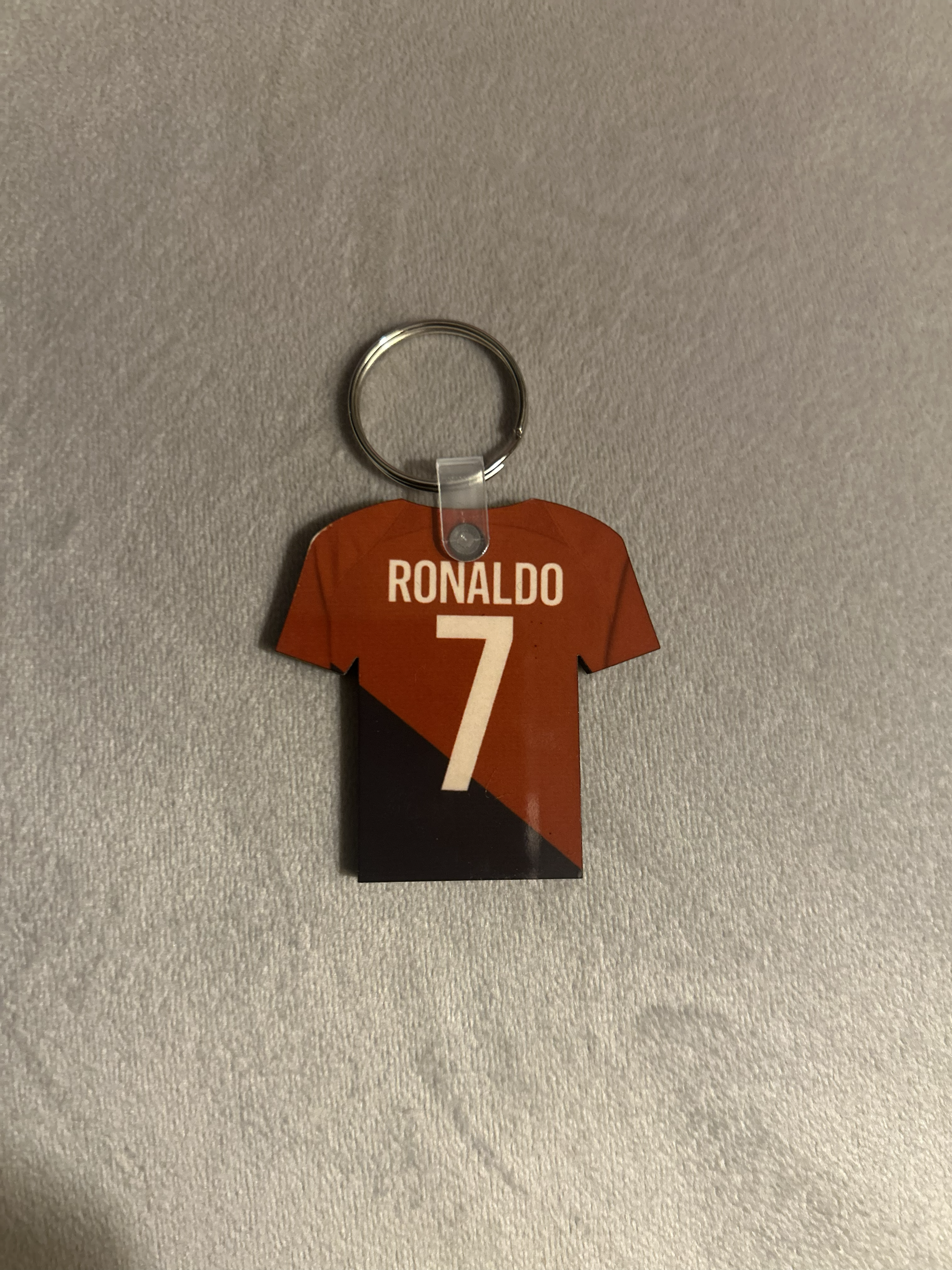 A keychain with a fake jersey of Cristiano Ronaldo, number 7, hanging on a textured gray surface.