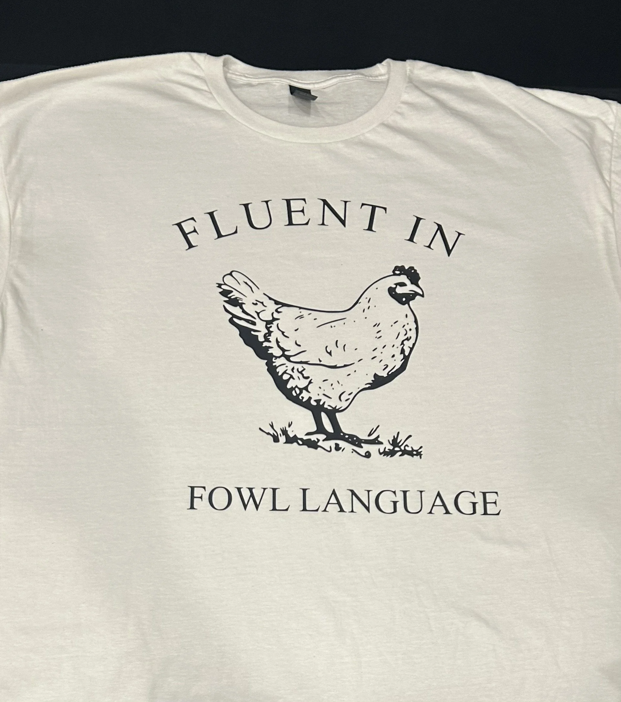 A white t-shirt with a graphic of a chicken and the words "Fluent in Fowl Language" printed on it.