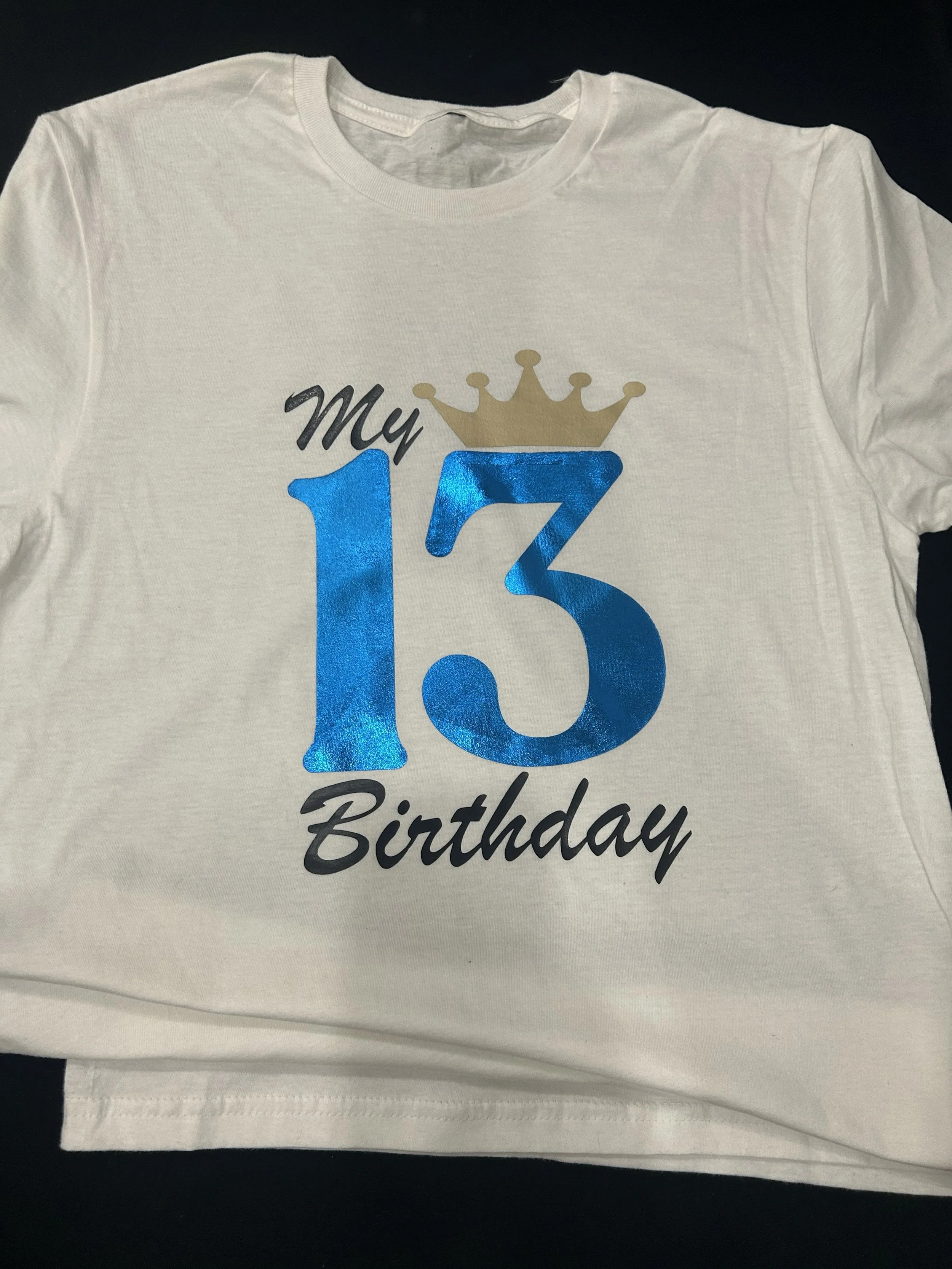 White T-shirt with a design that says 'My 13th Birthday' with a gold crown and the number 13 in blue.