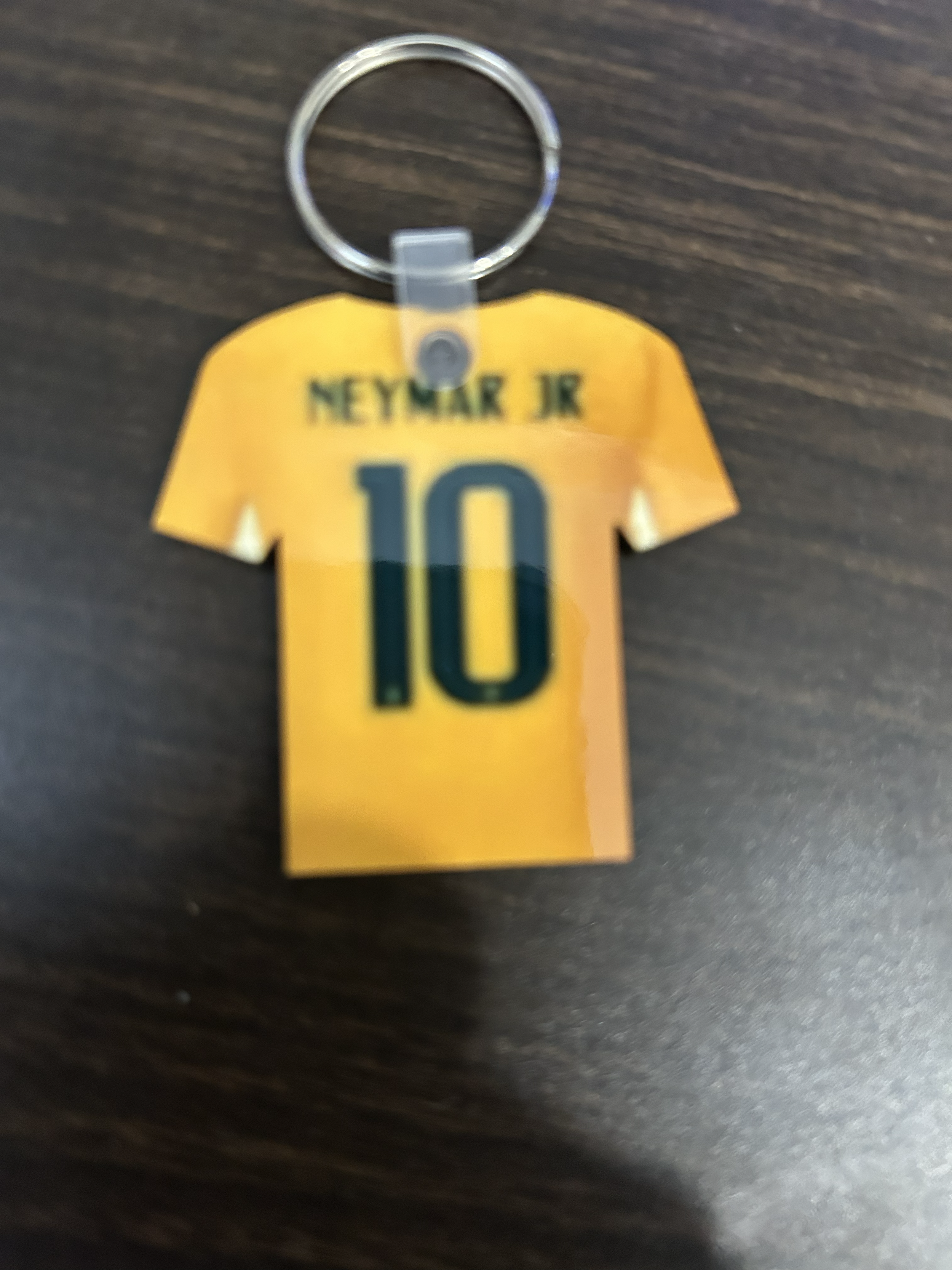 A keychain with a yellow shirt-shaped tag that has the name 'NEYMAR JR' and the number 10 printed on it, attached to a metal keyring.