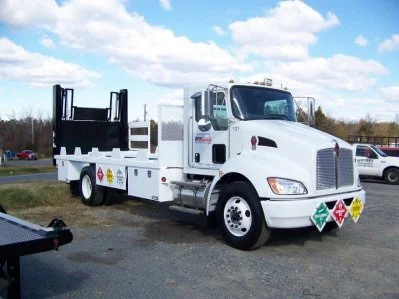 White service truck with safety and hazard signs parked outdoors on a gravel lot under a blue sky with clouds. Body paint job for a heavy truck fleet for a used truck company.