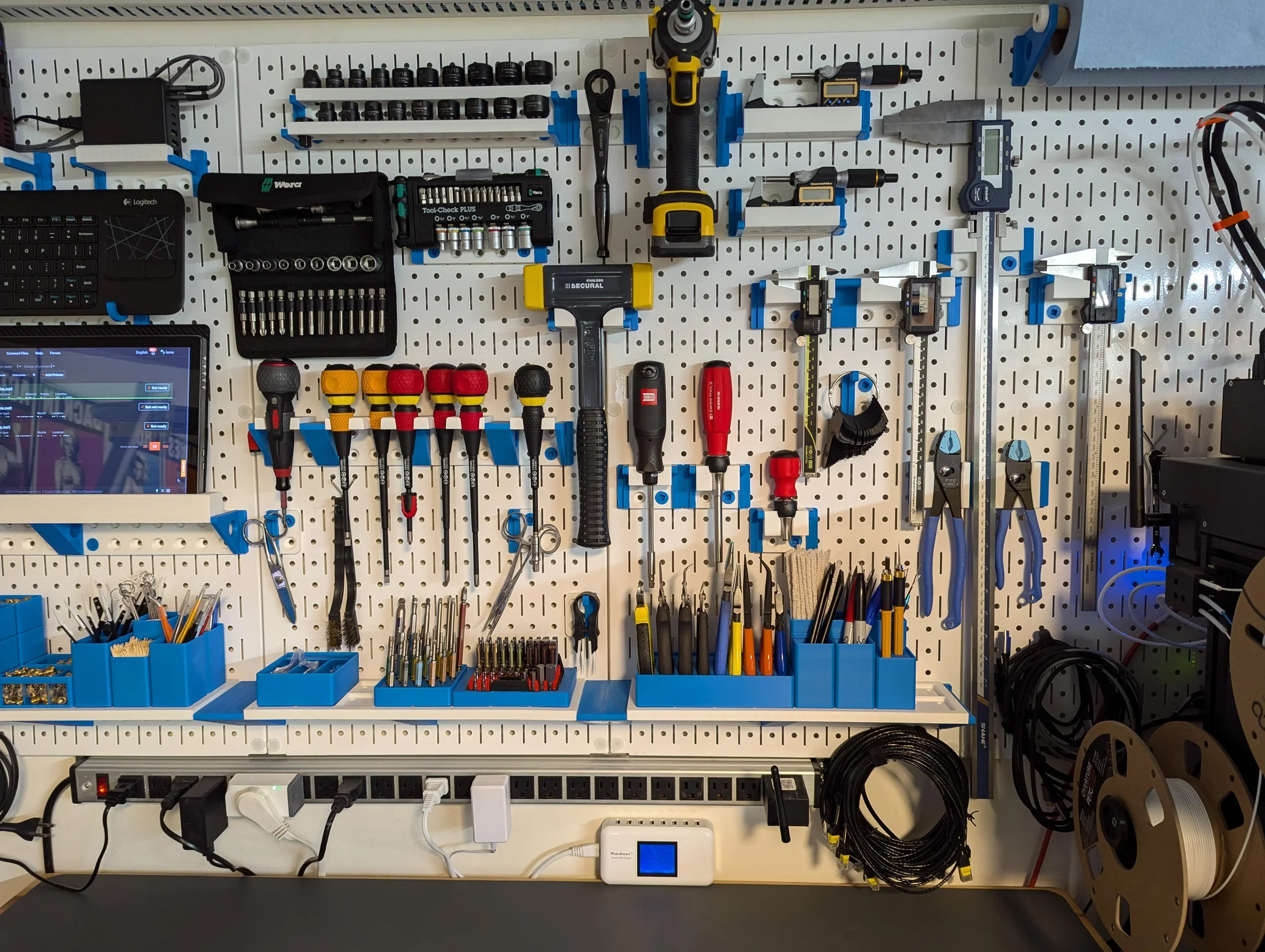 Organization of tools and equipment on a white pegboard with blue hooks, including screwdrivers, pliers, a digital caliper, a cordless drill, a digital multimeter, and power strips.