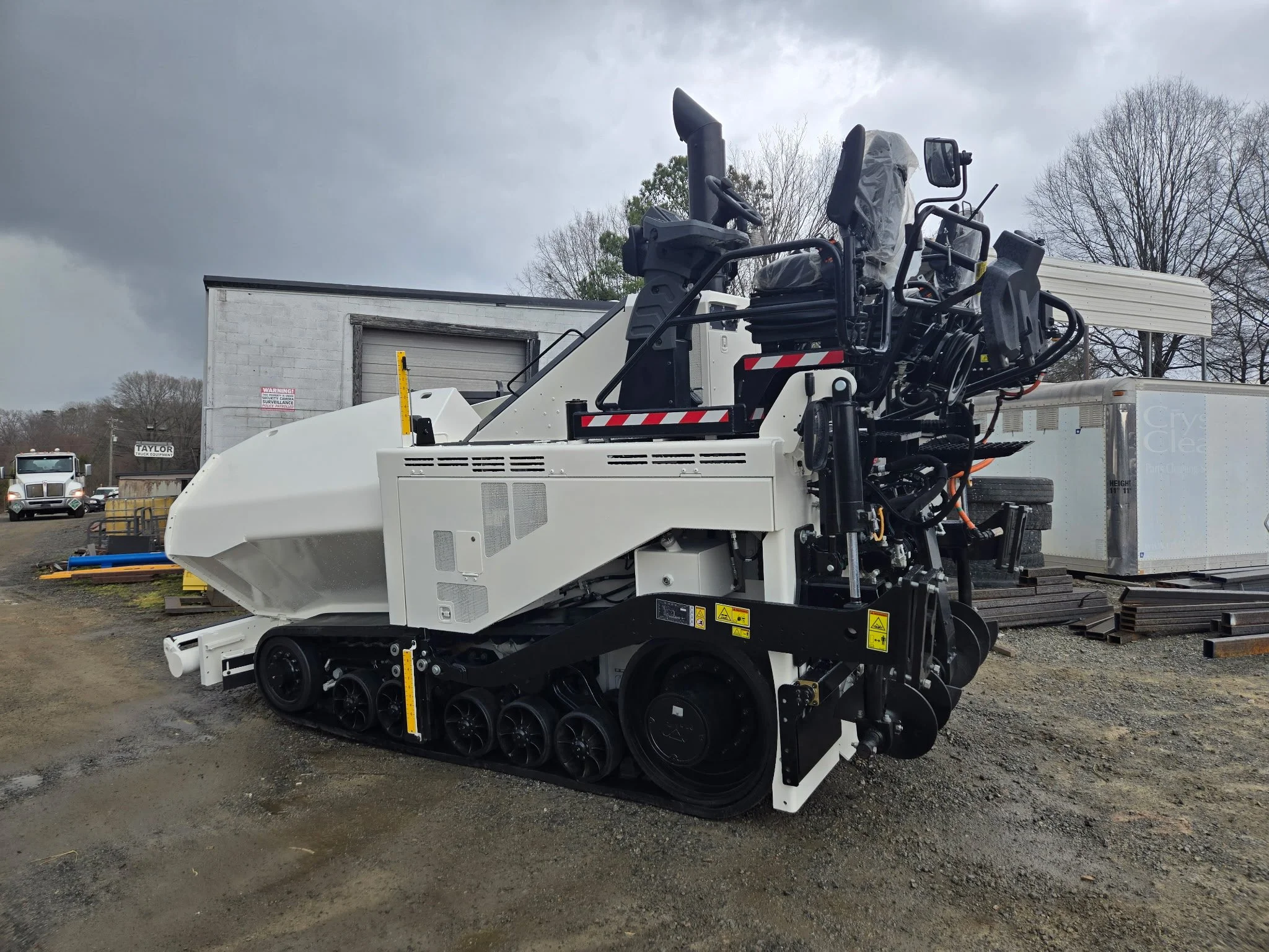 	
An asphalt paver machine with a large snowblower attachment, tracked wheels, and a control cabin, parked outdoors on a cloudy day. Body repair and body paint job for heavy equipment.