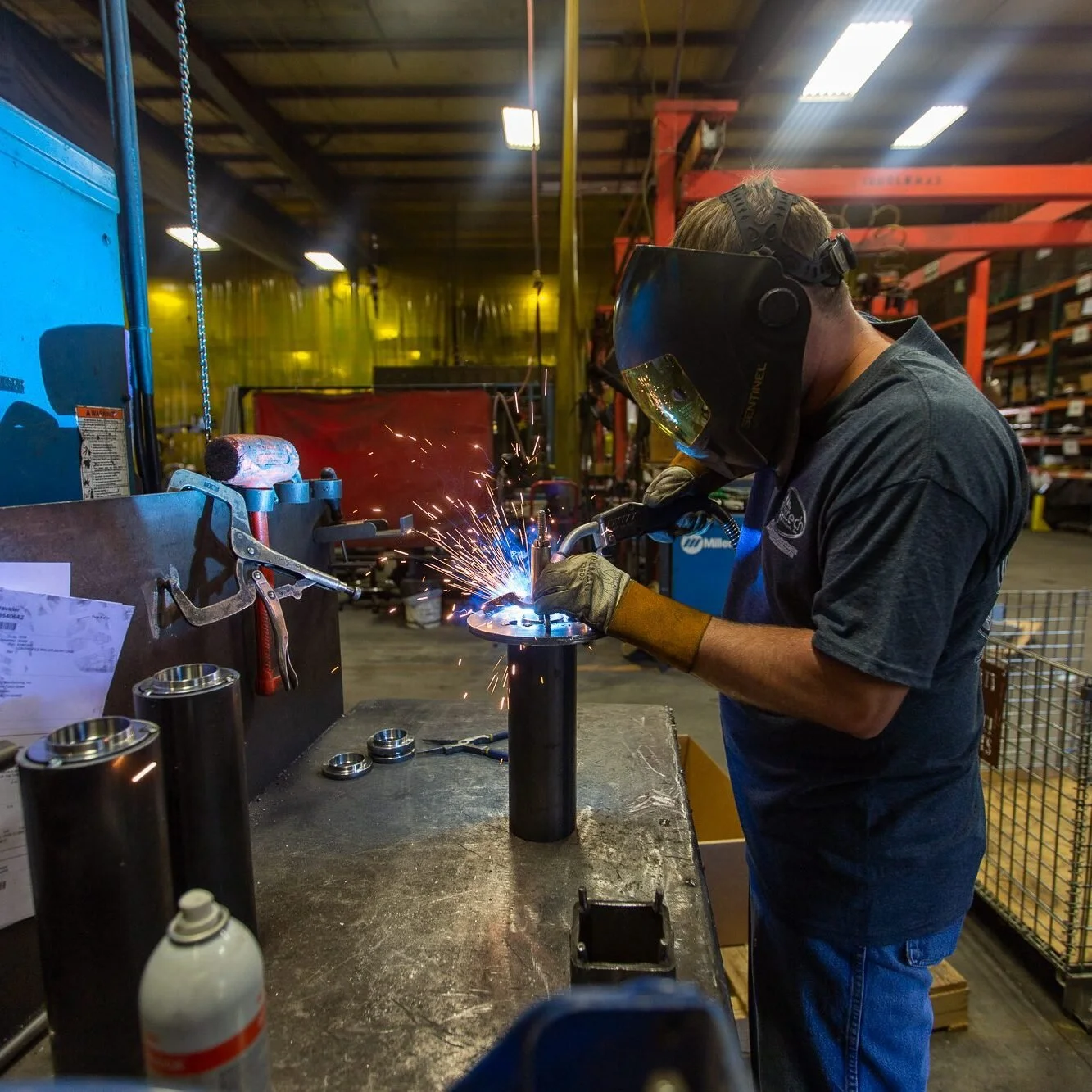 A worker welding metal parts in a manufacturing workshop, wearing protective gear including a helmet and gloves.