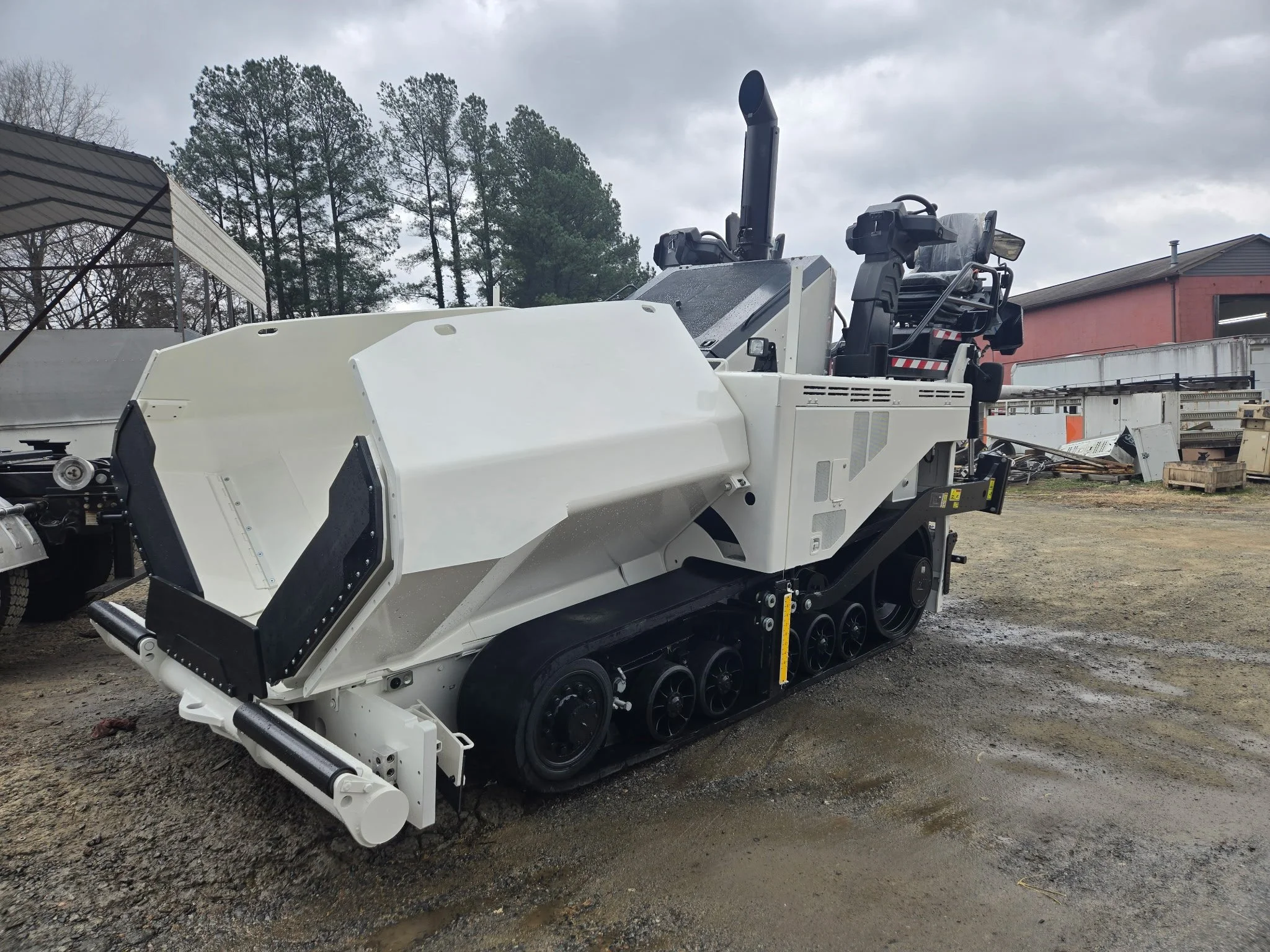 An asphalt paver machine with a large snowblower attachment, tracked wheels, and a control cabin, parked outdoors on a cloudy day. Body repair and body paint job for heavy equipment.