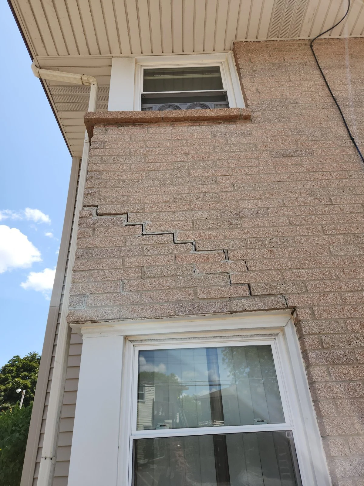 Stair-step crack through the mortar joints of brick veneer, running from the corner above a lower window.