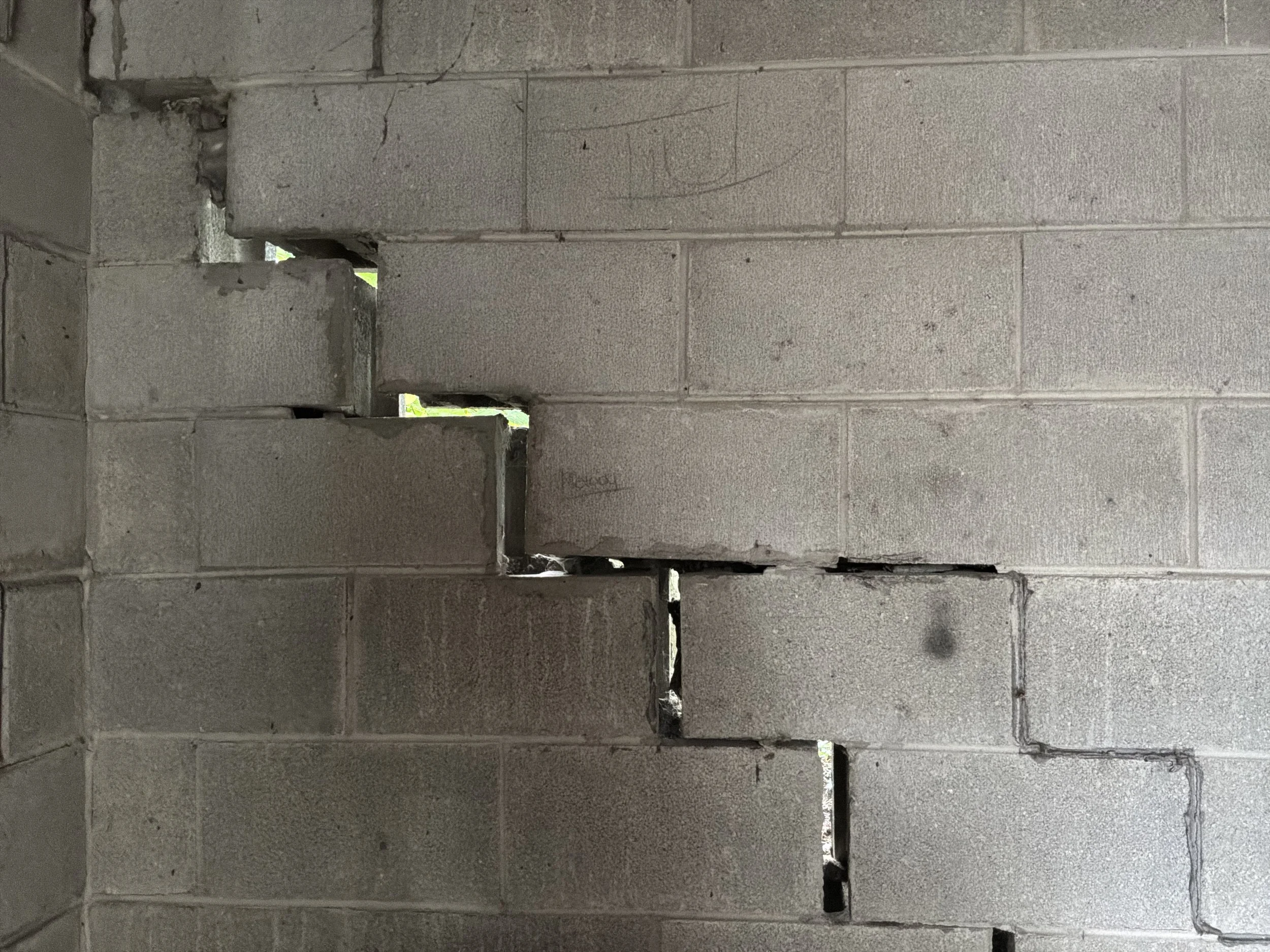 Stepped diagonal crack through a block foundation wall, tapered and displaced, with daylight visible through the separation