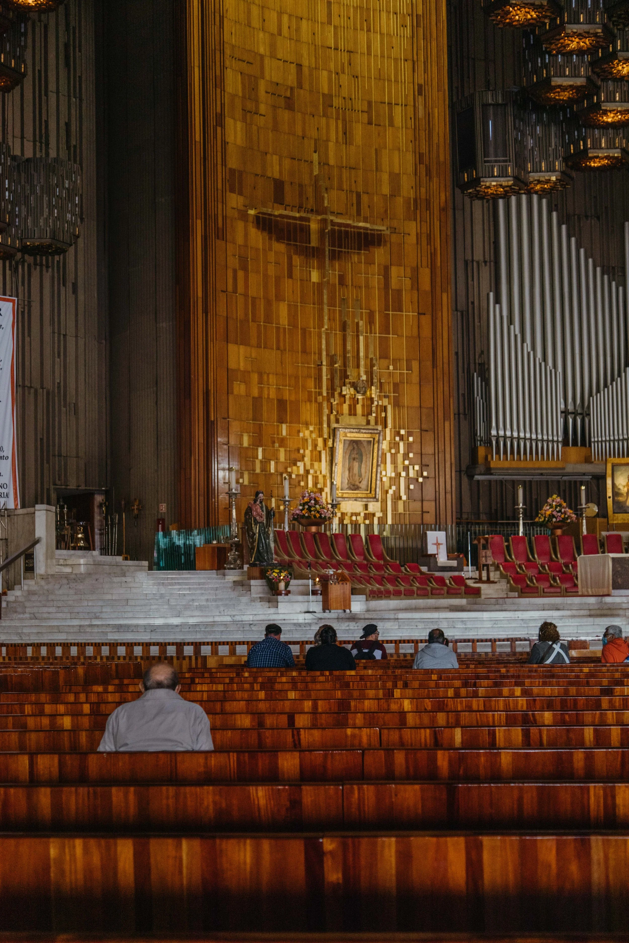 Interior of a Catholic church with wooden pews, an altar with a crucifix, flowers, and religious statues, and a large organ on the right side.