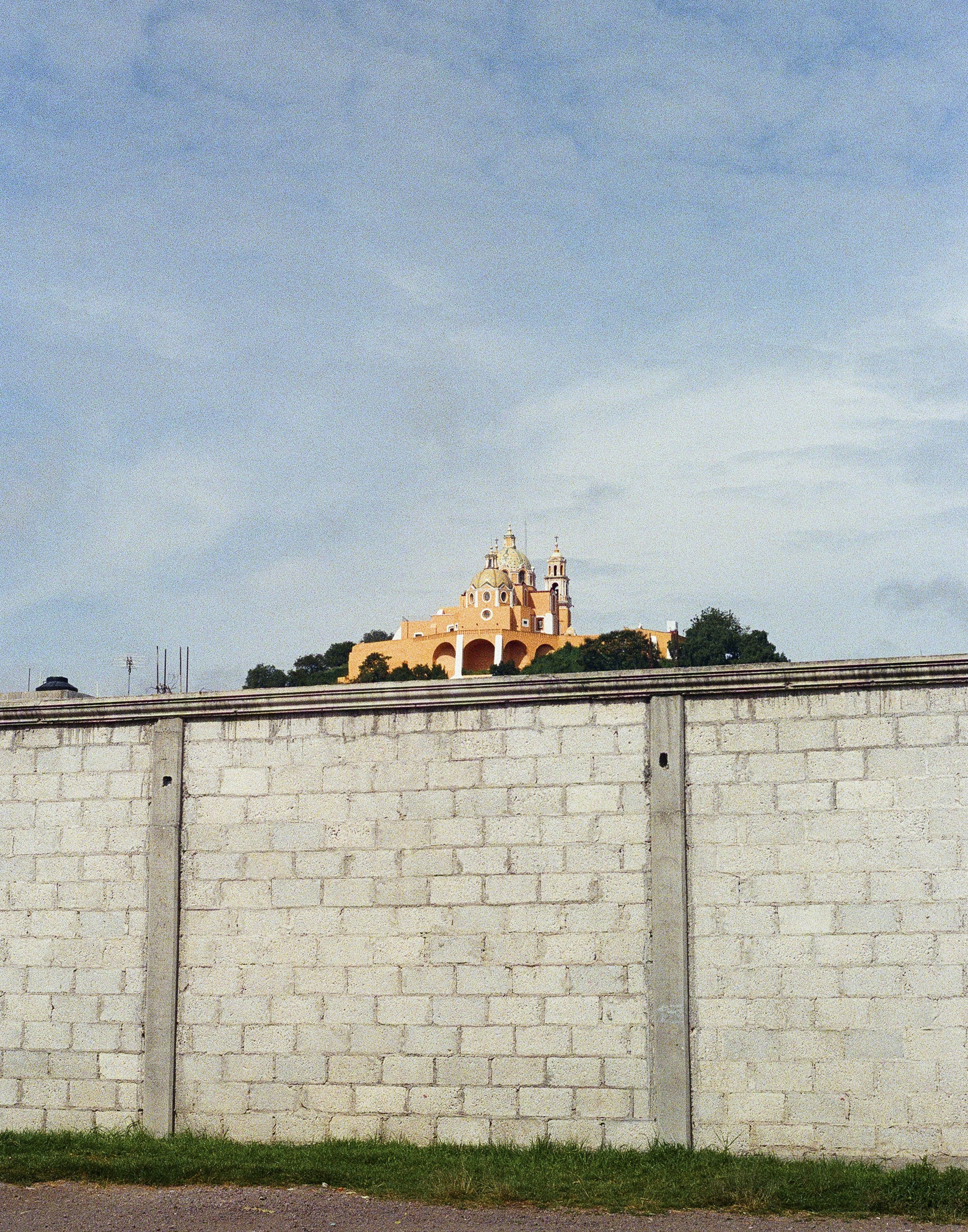 Church on a hill viewed from behind a concrete wall, with a cloudy sky above