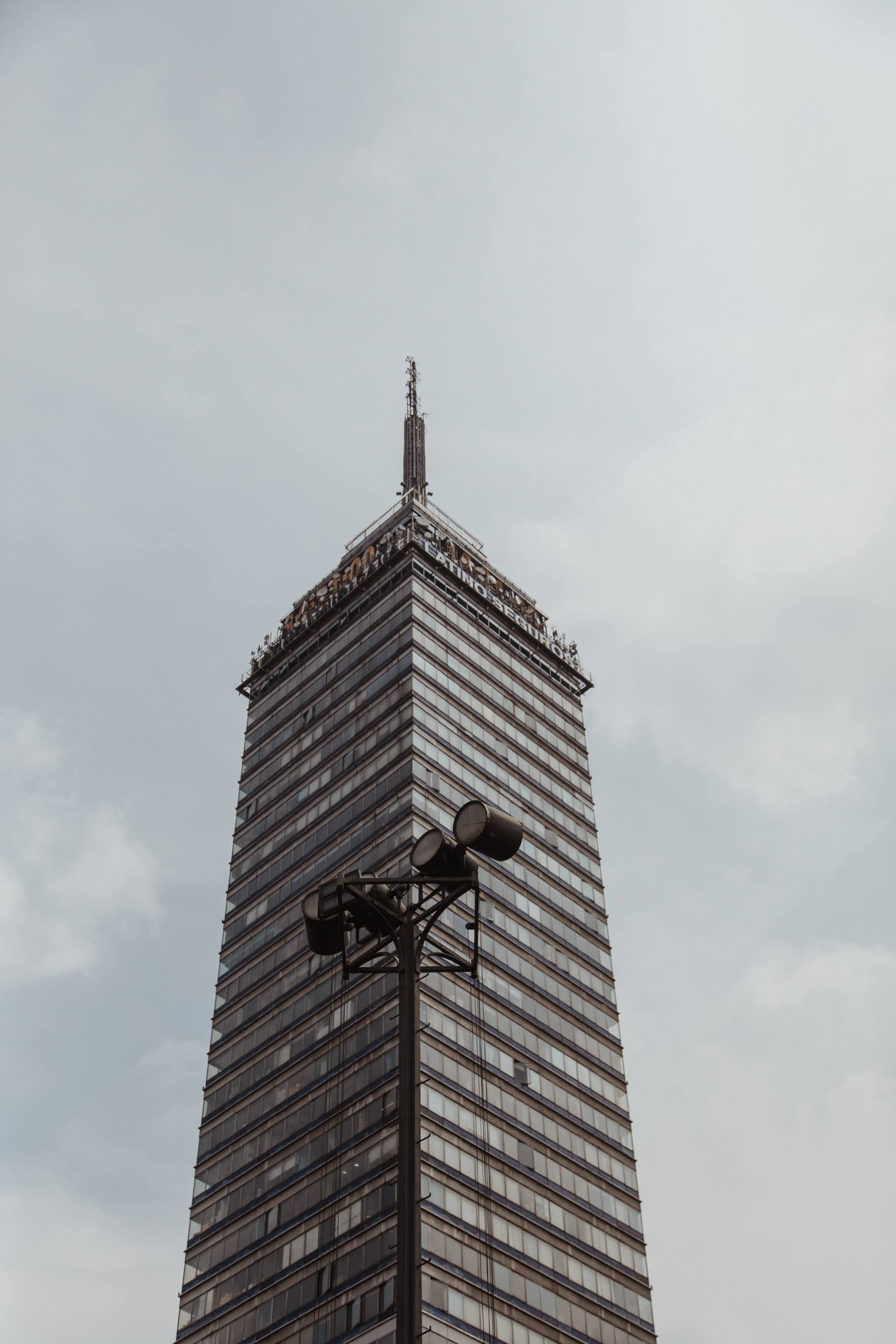 A tall skyscraper with a pointed antenna on top, viewed from below on a cloudy day.