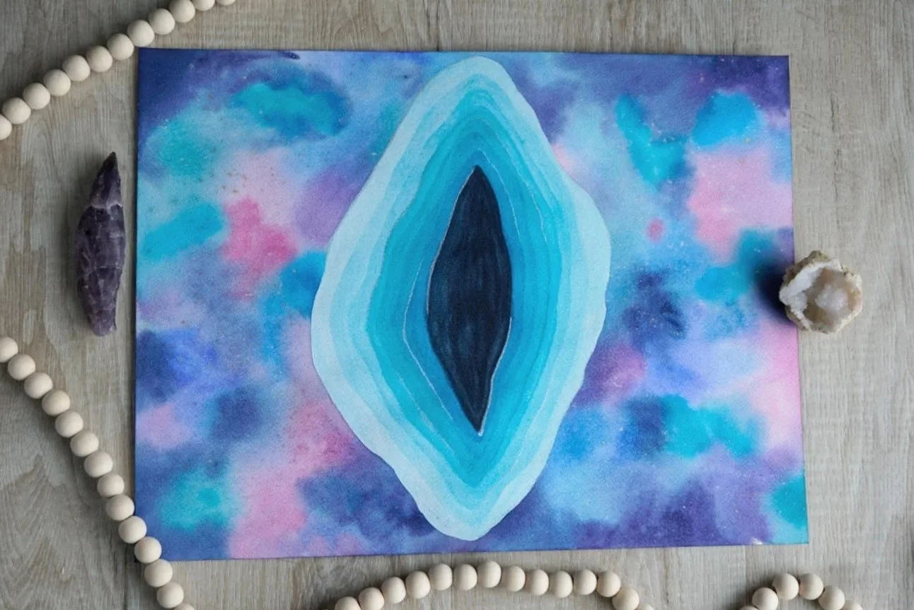 A painting of an abstract blue and black eye shape on a colorful, cosmos-like background with surrounding crystals and beads.