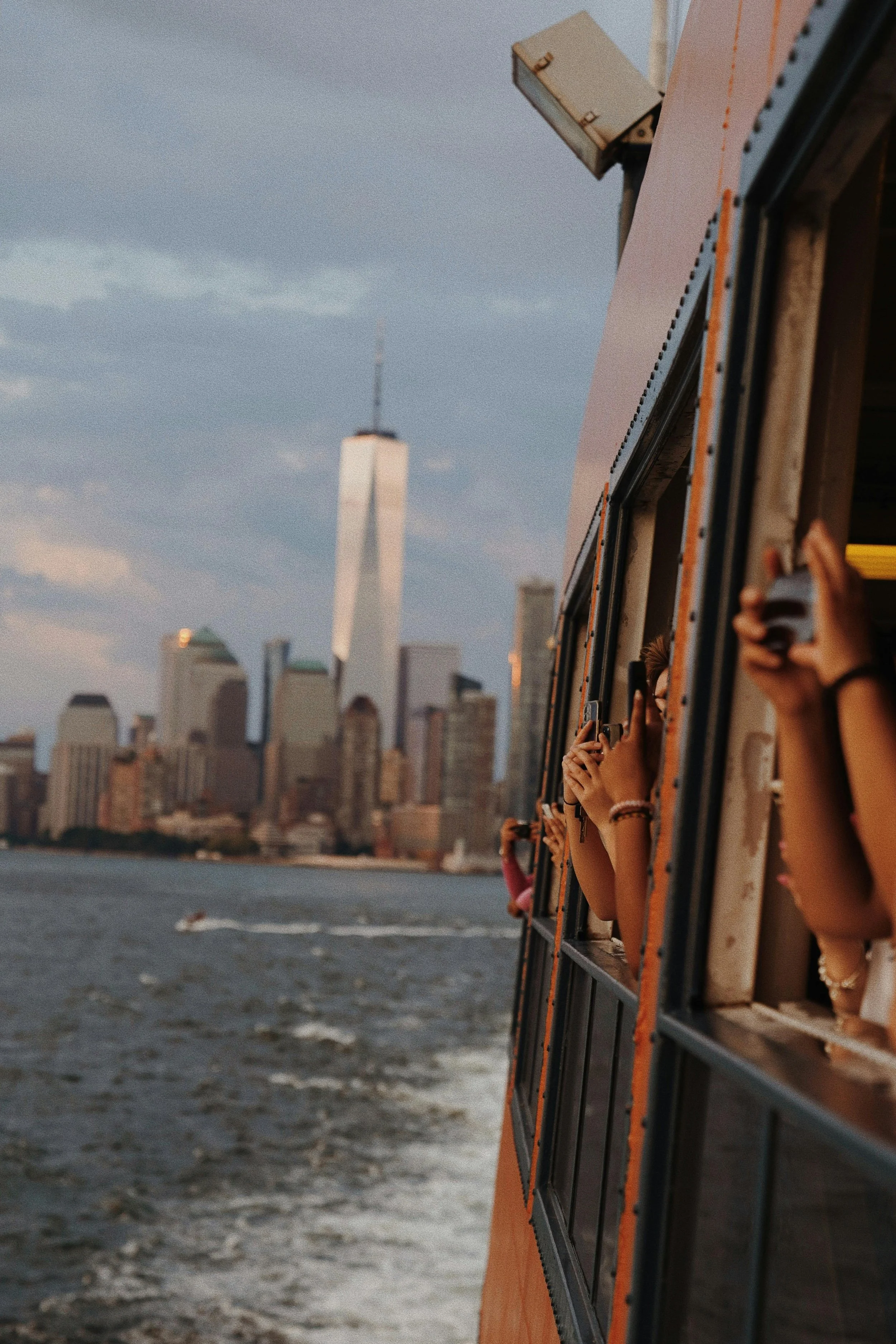 People looking out from the window of the Staten Island Ferry as it travels along the harbor in New York City with the Manhattan skyline, including One World Trade Center, in the background.