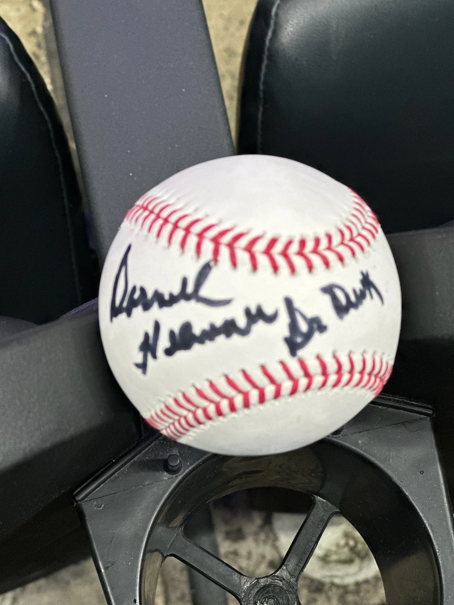 A signed baseball resting on a black wheelchair armrest.
