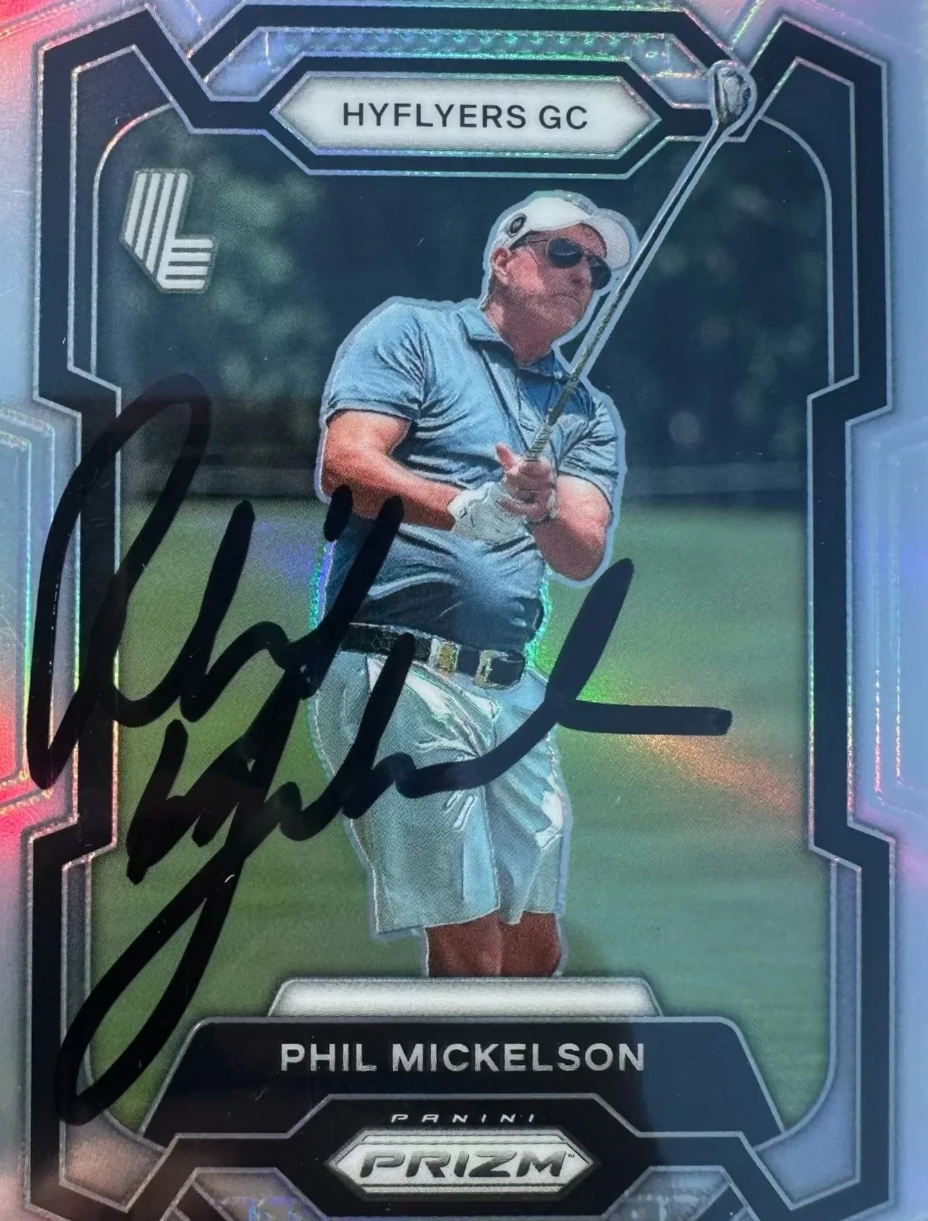 Autographed sports card featuring Phil Mickelson, a golfer, in a blue golf shirt and white cap, holding a golf club, with a green golf course background and 'HYFLYERS GC' at the top.
