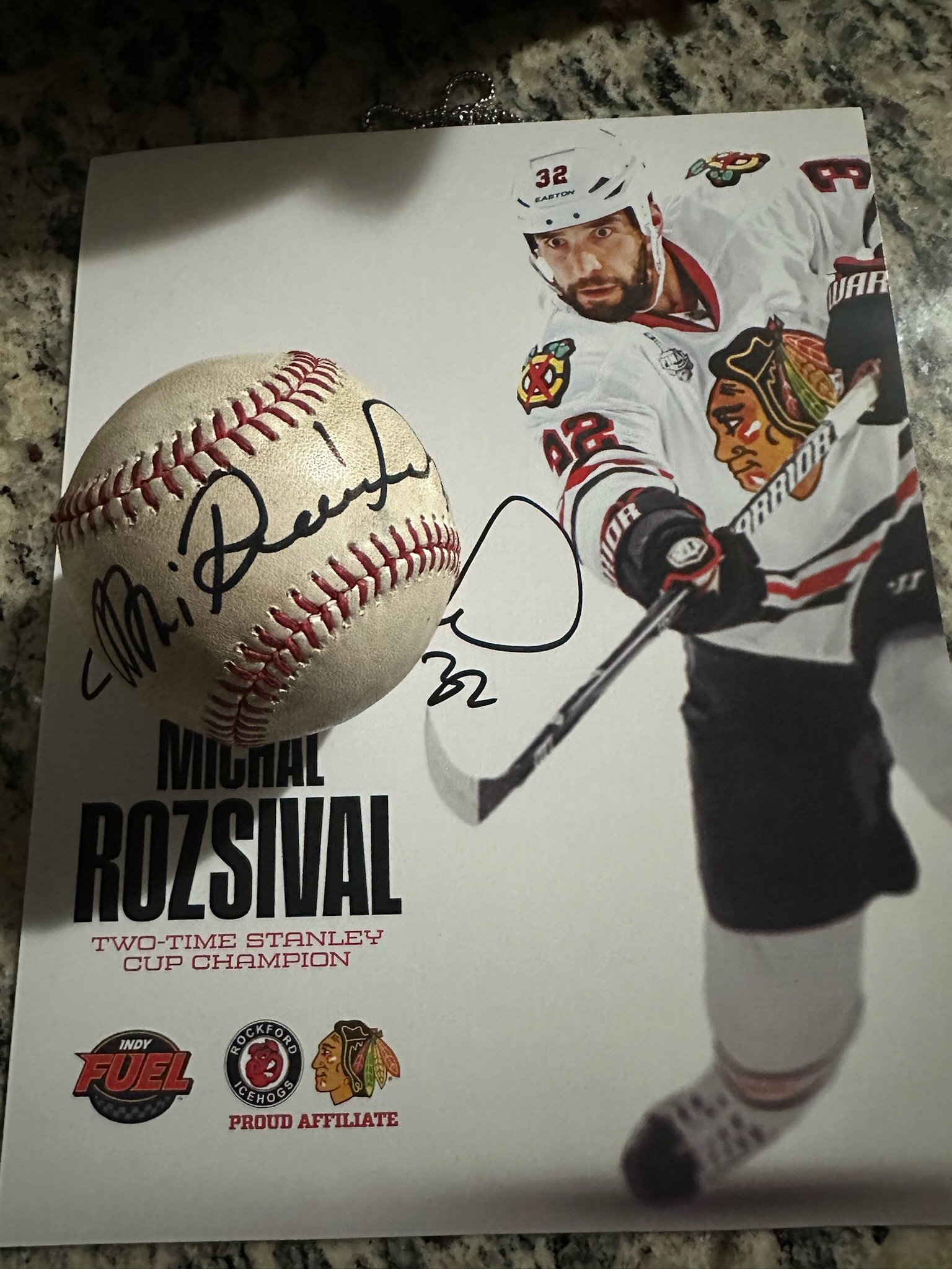 Autographed baseball with a stamp and image of an ice hockey player in a white Chicago Blackhawks jersey on a poster celebrating the NHL's Michigan Rozsival as a two-time Stanley Cup champion.