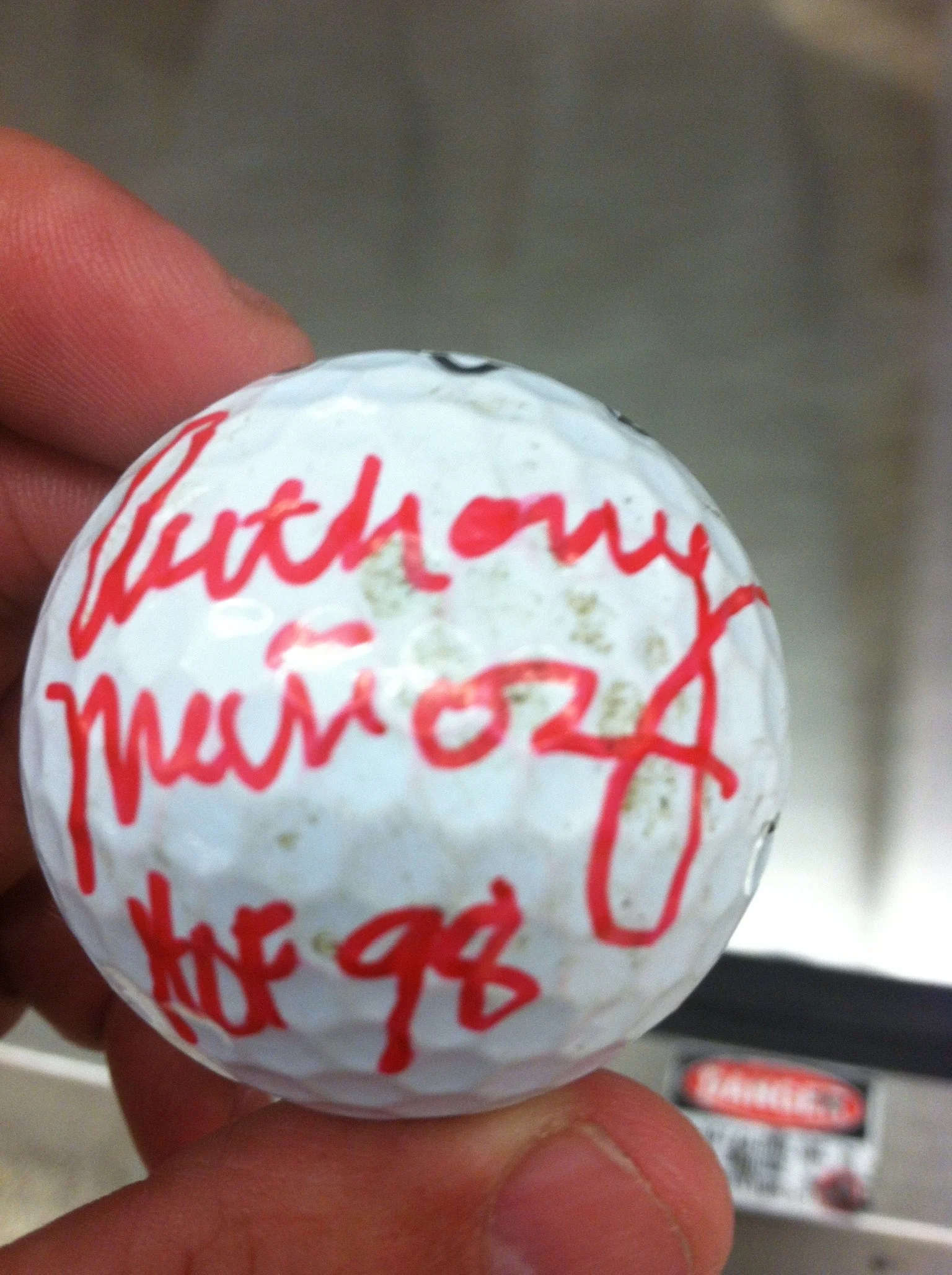 A golf ball with red handwritten text, including the date 10/24 and handwritten message.
