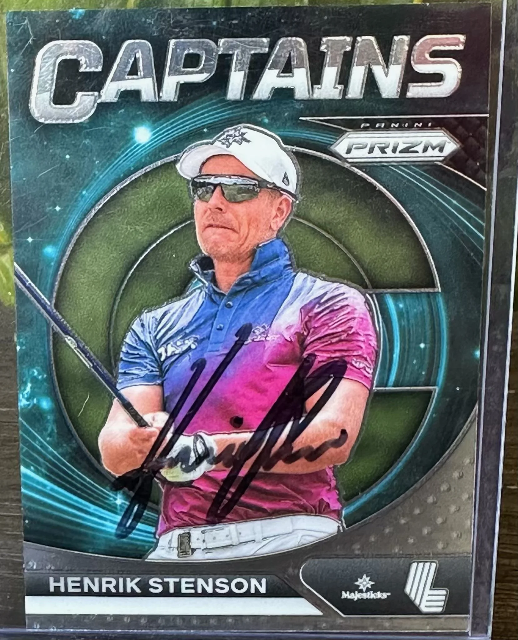 A trading card of Henrik Stenson with a signature, featuring him in a blue and pink golf outfit, sunglasses, and holding a golf club.