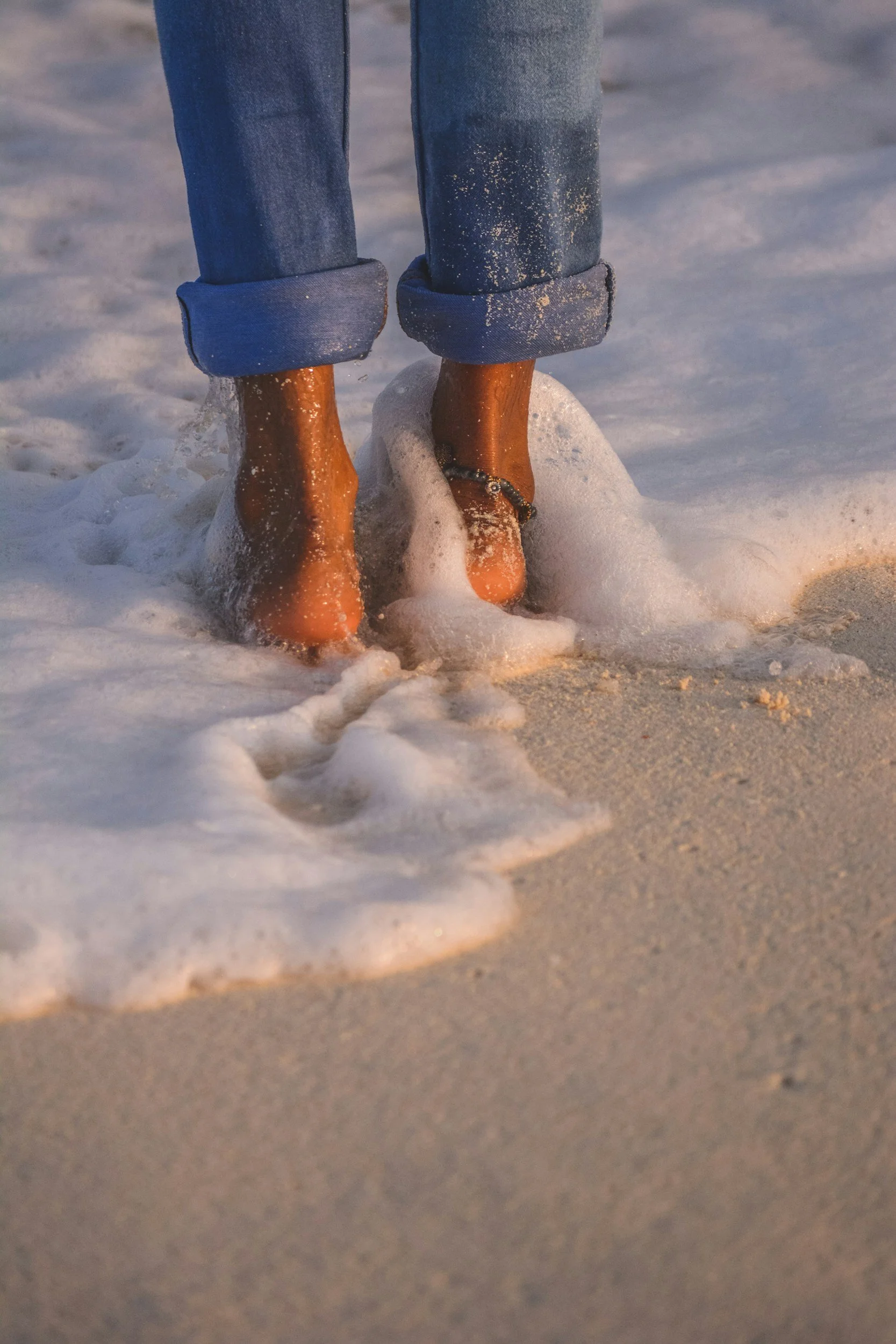 Feet standing where the ocean meets the sand