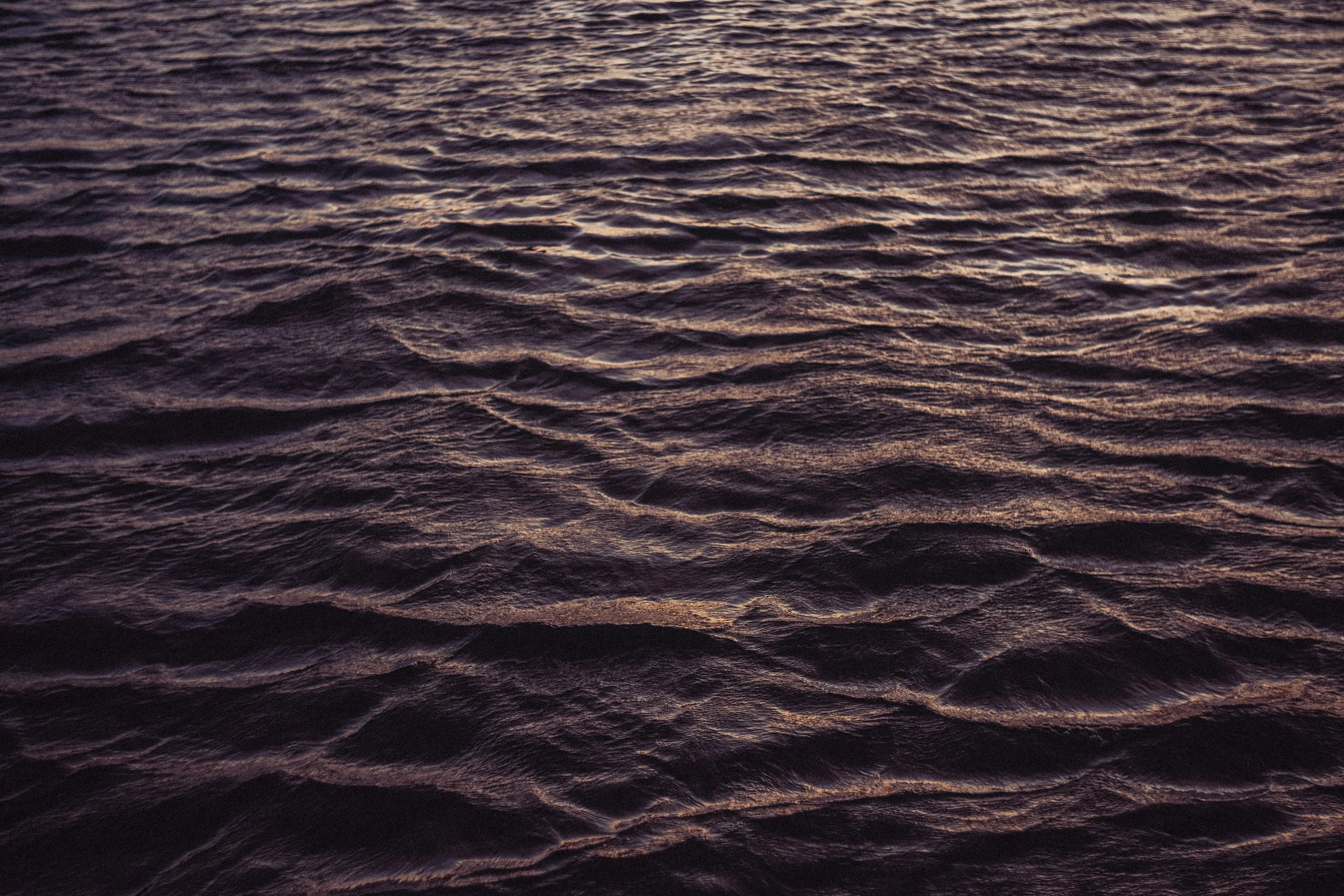Dark ocean water with small waves, reflecting a soft pinkish-purple hue from the sunset or sunrise.